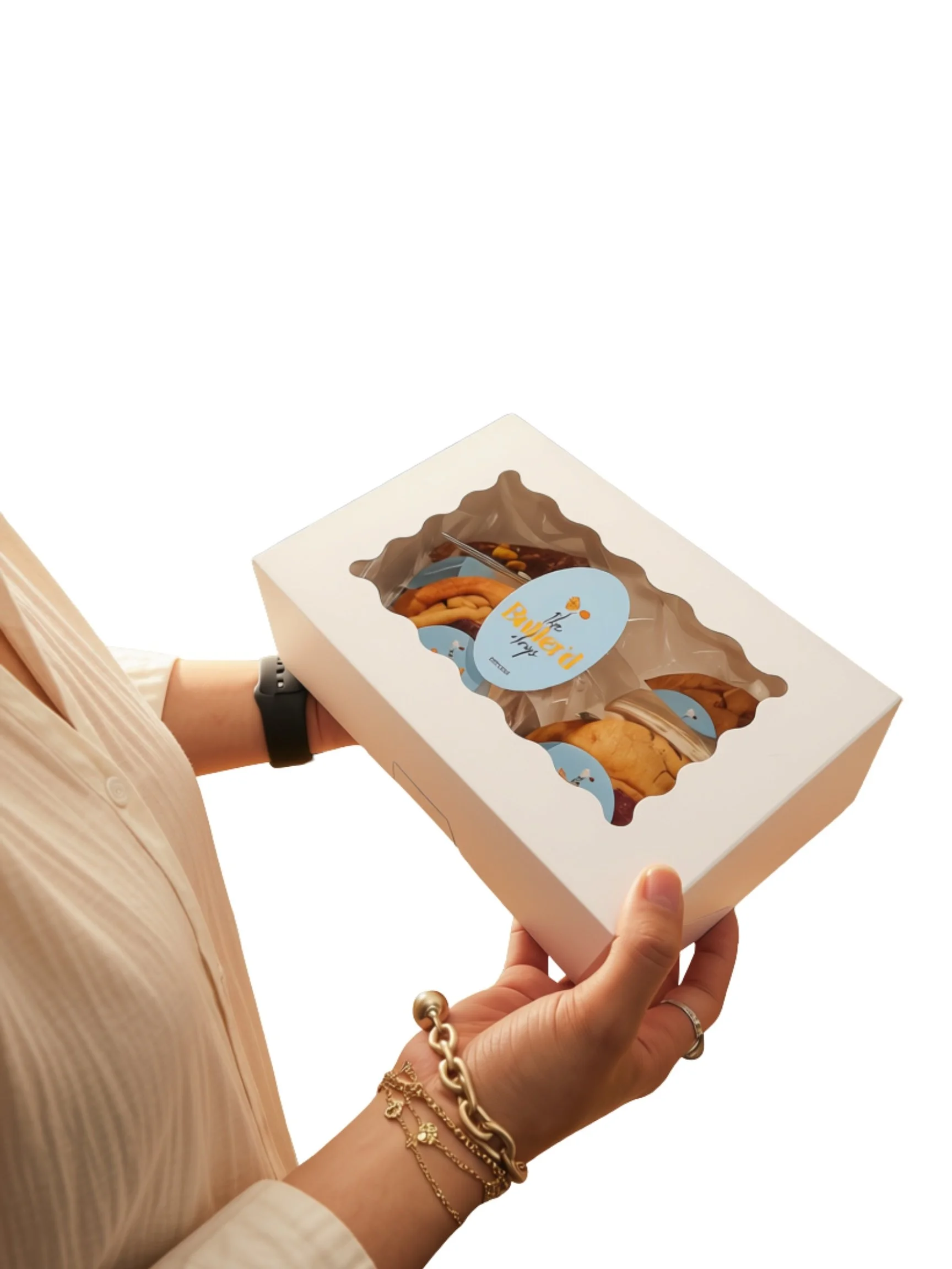 A person holding a white box with a clear window showcasing cookies and a blue label that says "the butterfly". The person is wearing a white shirt and gold jewelry on their wrist.