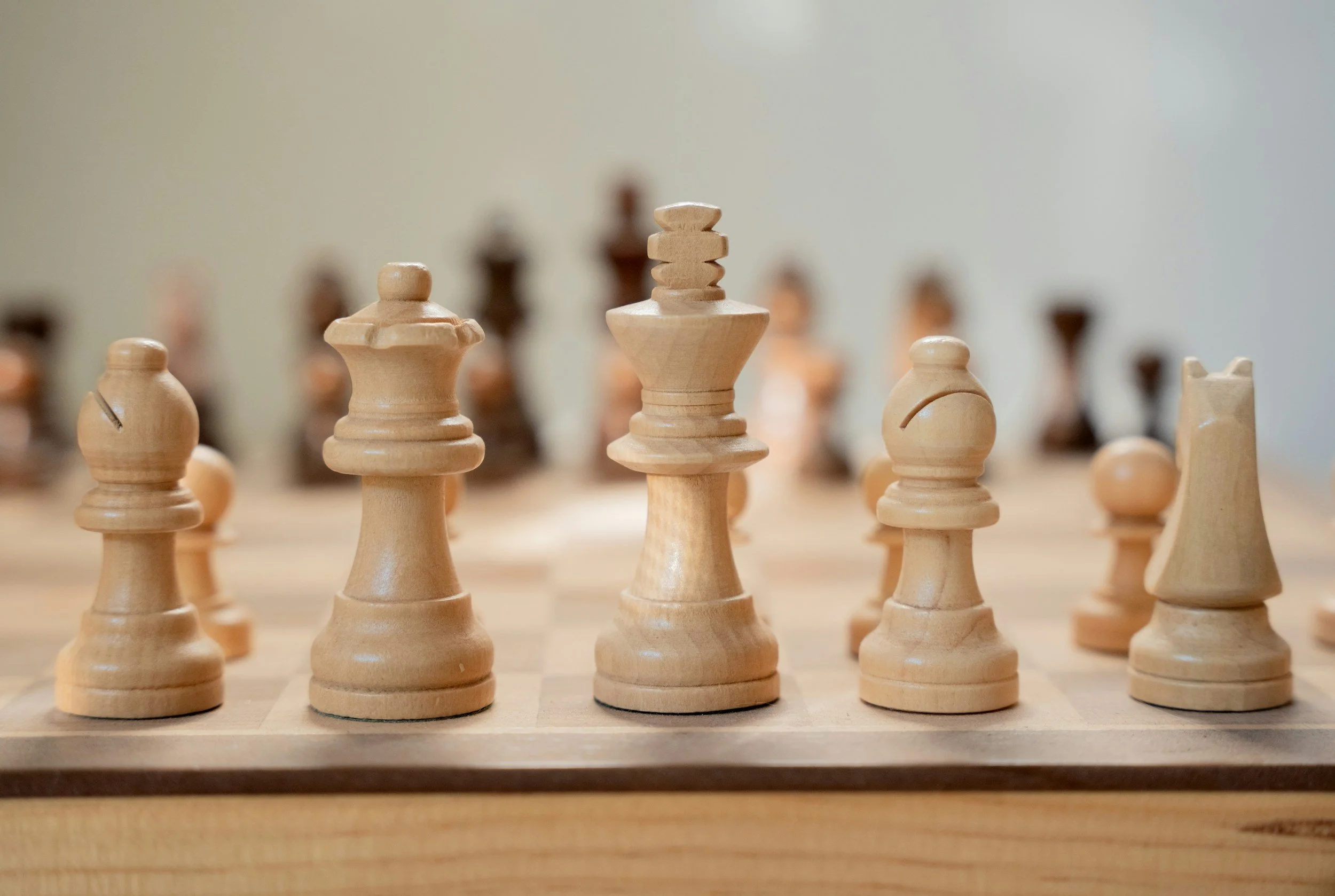 Nahaufnahme eines Schachbretts mit Holzfiguren, im Fokus die Figuren König, Dame und Springer.