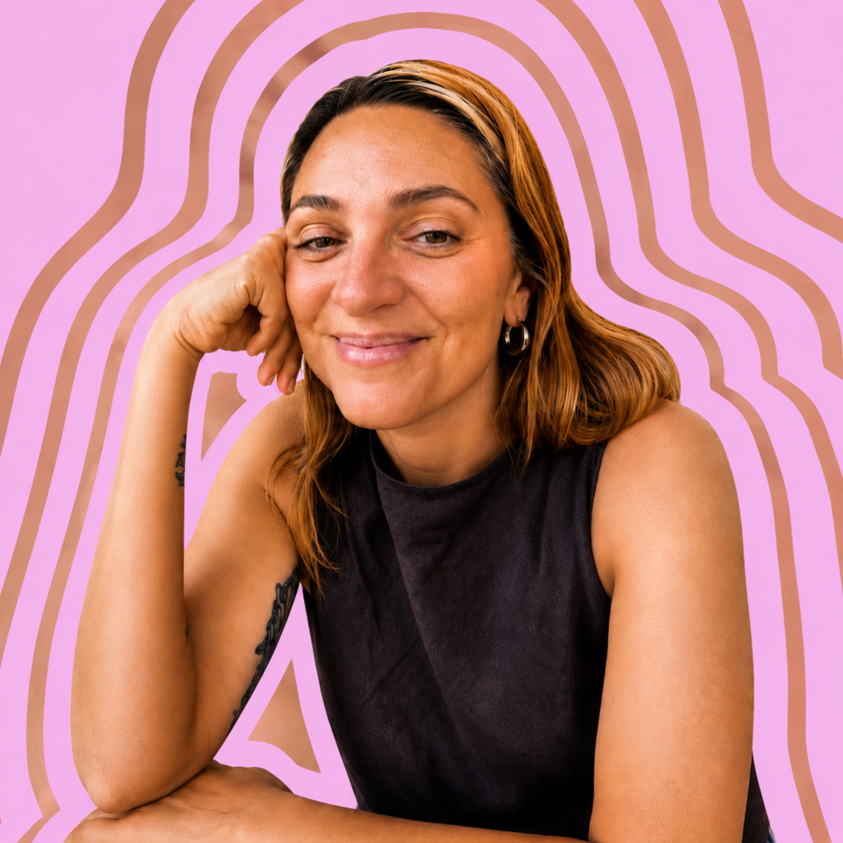 A woman with ginger hair and a black sleeveless top smiling and resting her head on her left hand. She has a tattoo on her right forearm and wears earrings. The background has pink color with brown curved lines.