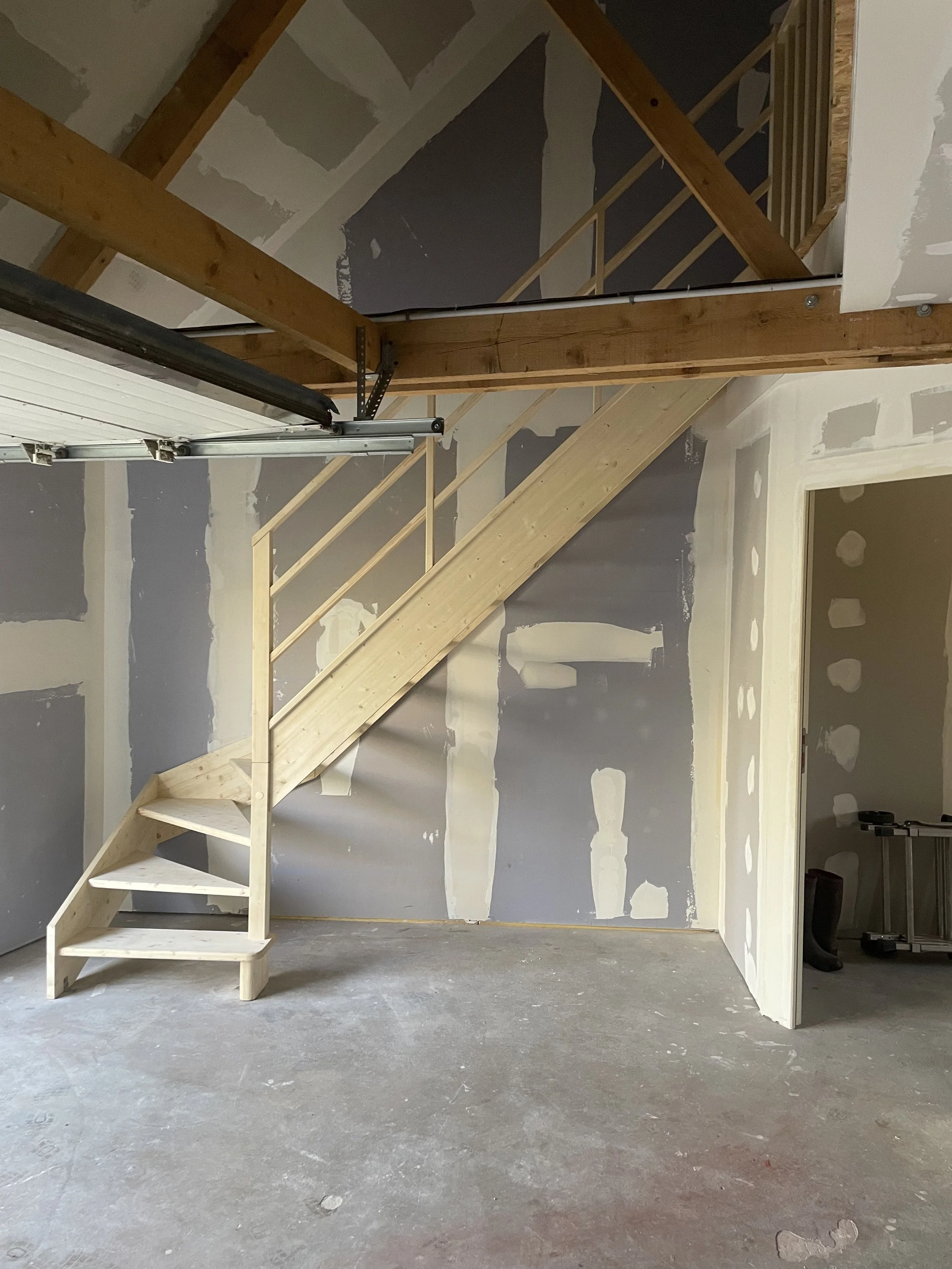 Escalier en bois non fini dans une pièce en construction avec murs en plaques de plâtre non peints.