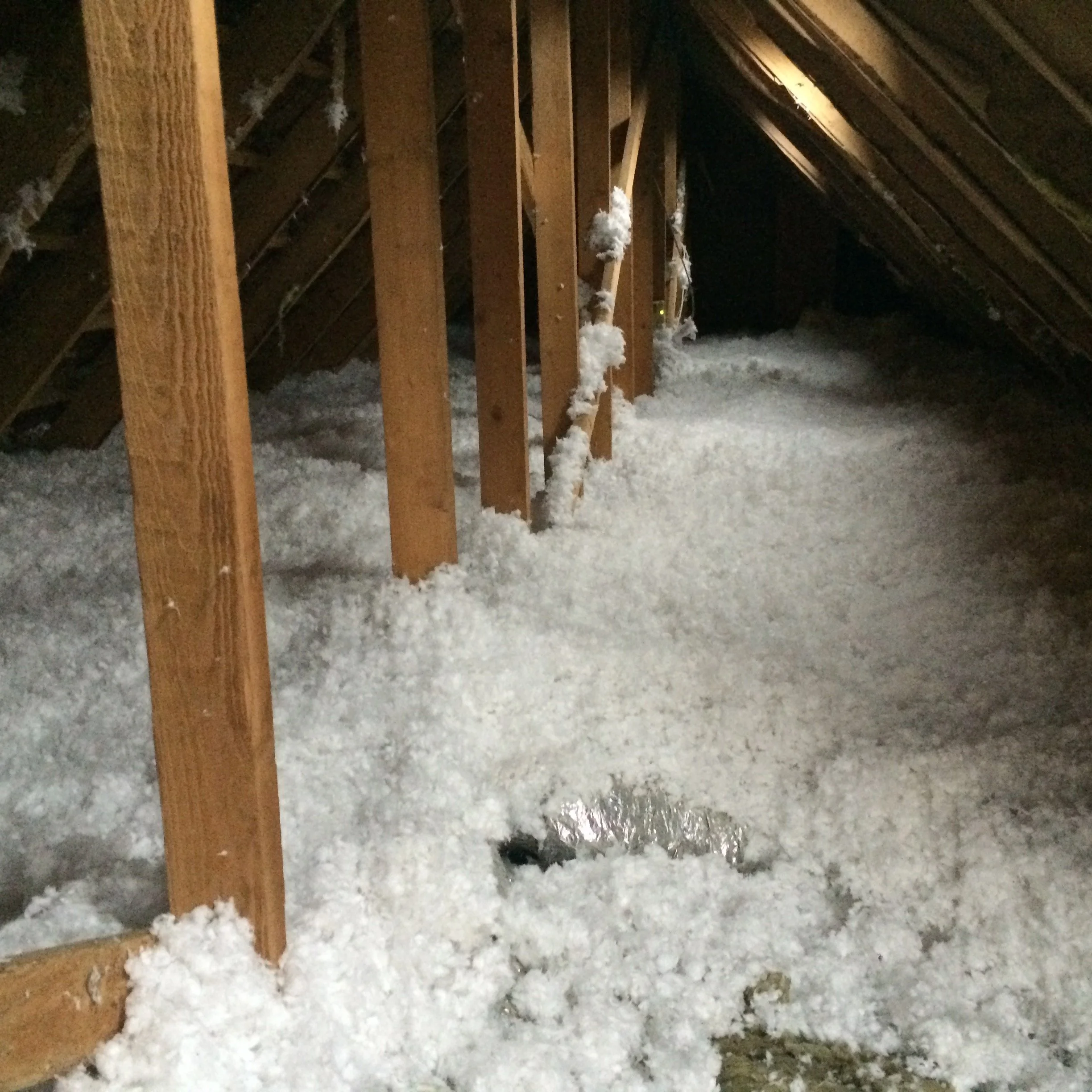 Sol enneigé dans un espace sous comble avec des poutres en bois et des morceaux de coton ou de ouate accumulés.
