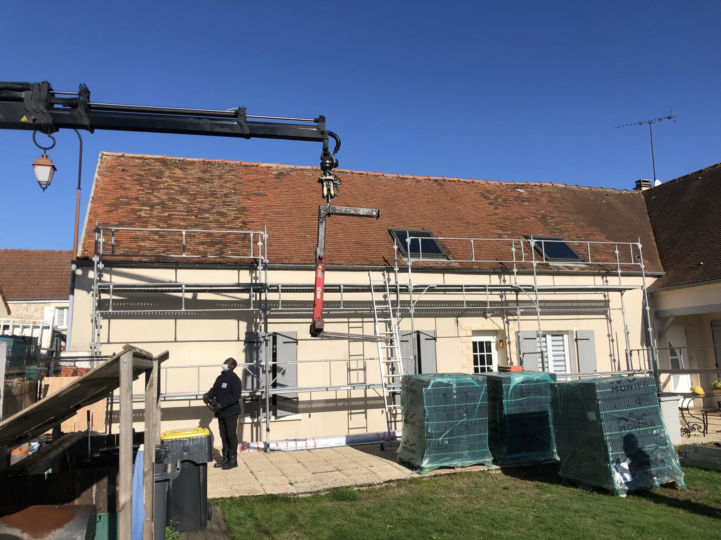 Construction de toiture sur une maison avec échelle et matériaux de couverture, ouvrier en train de travailler.
