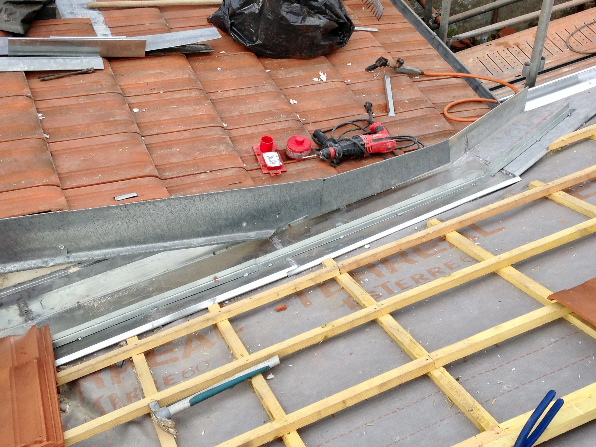 Transformation de charpente d'une maison, avec des outils posés dessus, entourée d'une maison en pierre. 