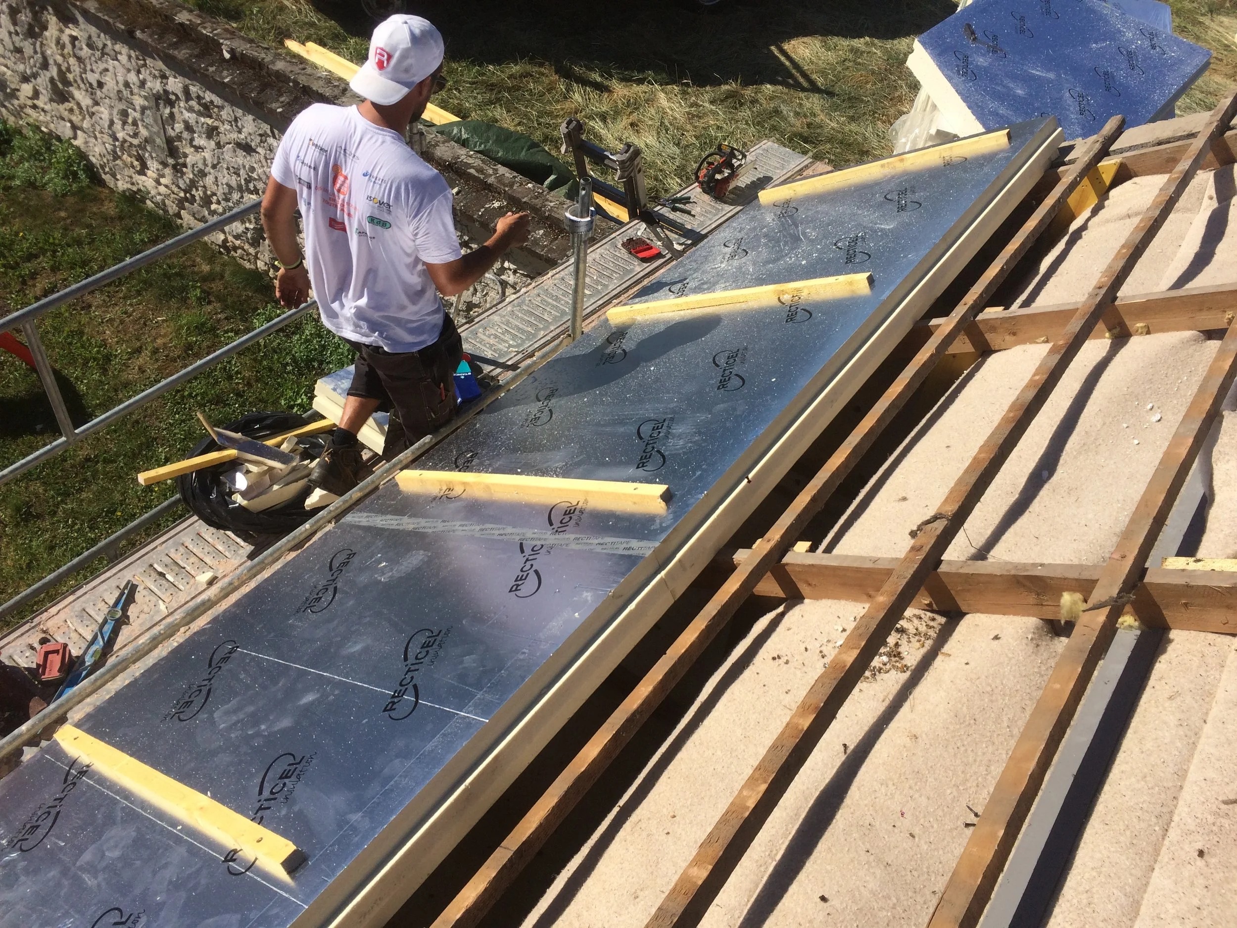Un homme travaillant sur une toiture en construction, utilisant des outils et une isolation réfléchissante.