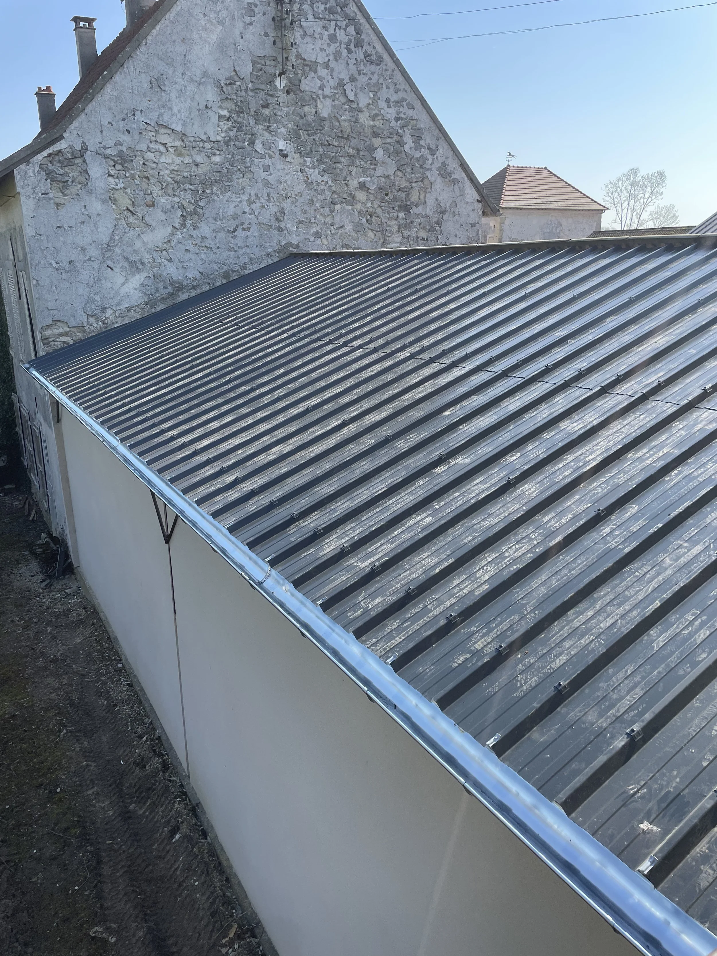 Une vue d'un bâtiment avec un toit en tôle ondulée métallique et un mur en pierre existant à l'arrière, sous un ciel clair