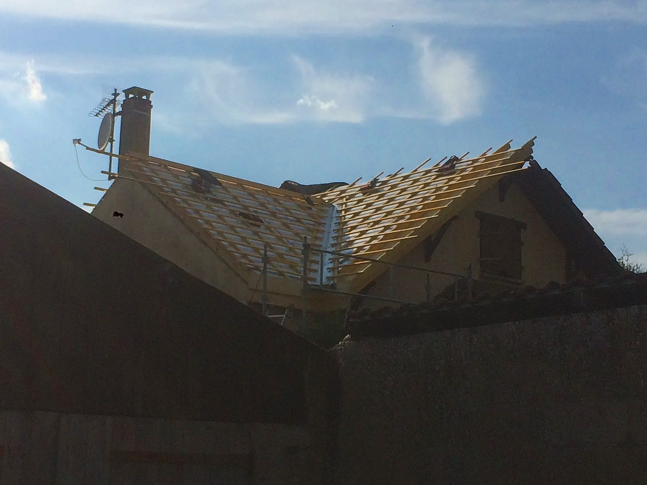 Toit en cours de construction avec des tuiles en bois et une cheminée, ciel bleu avec quelques nuages.