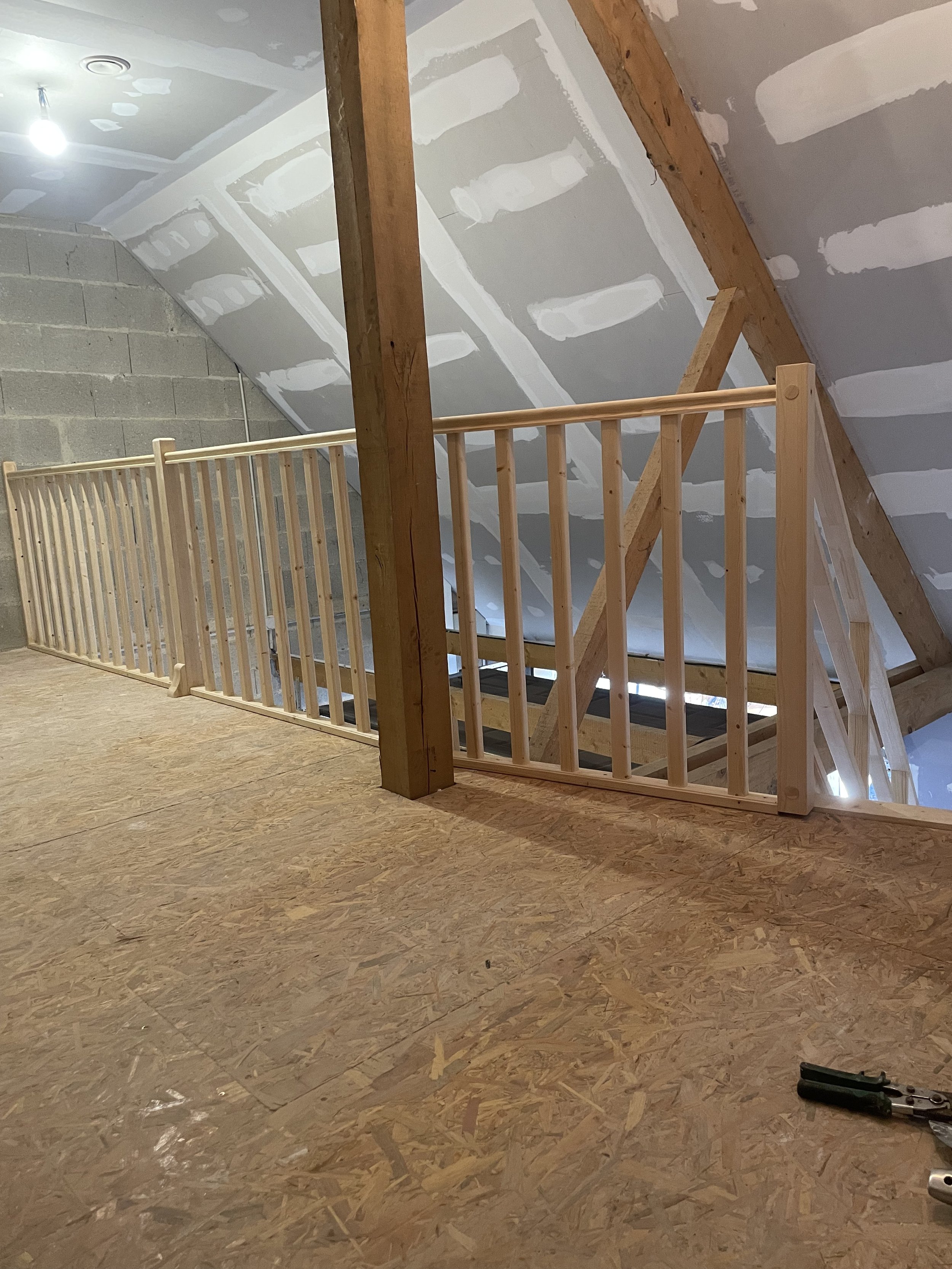 Intérieur d'une pièce en construction ou en rénovation avec un plafond en placo à finir, un sol en bois pressé, une clôture en bois, une poutre en bois et des outils de bricolage sur le sol.