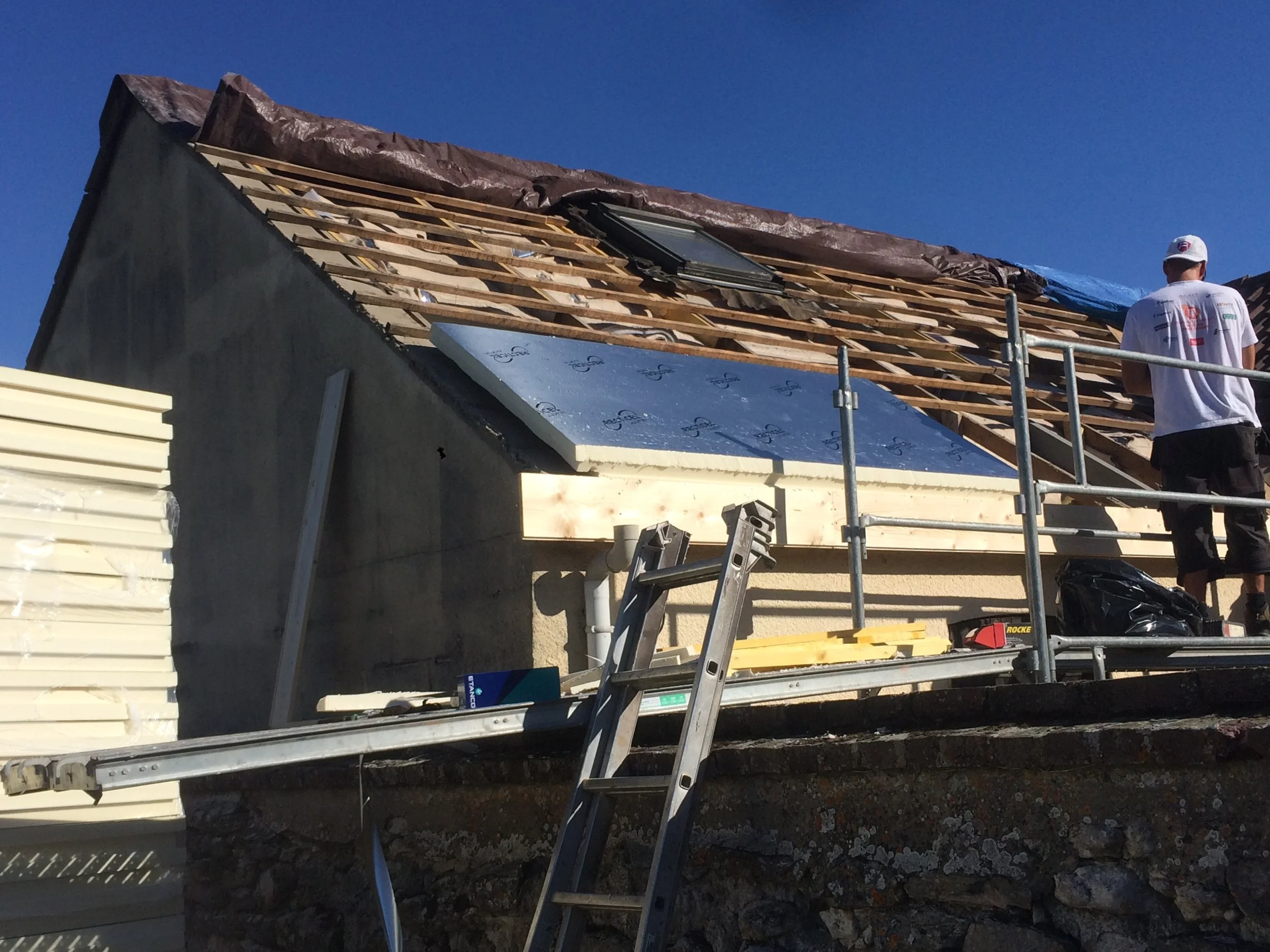Construction d'une toiture avec une fixations pour panneau solaire en cours, ouvrier observant, ciel bleu clair.