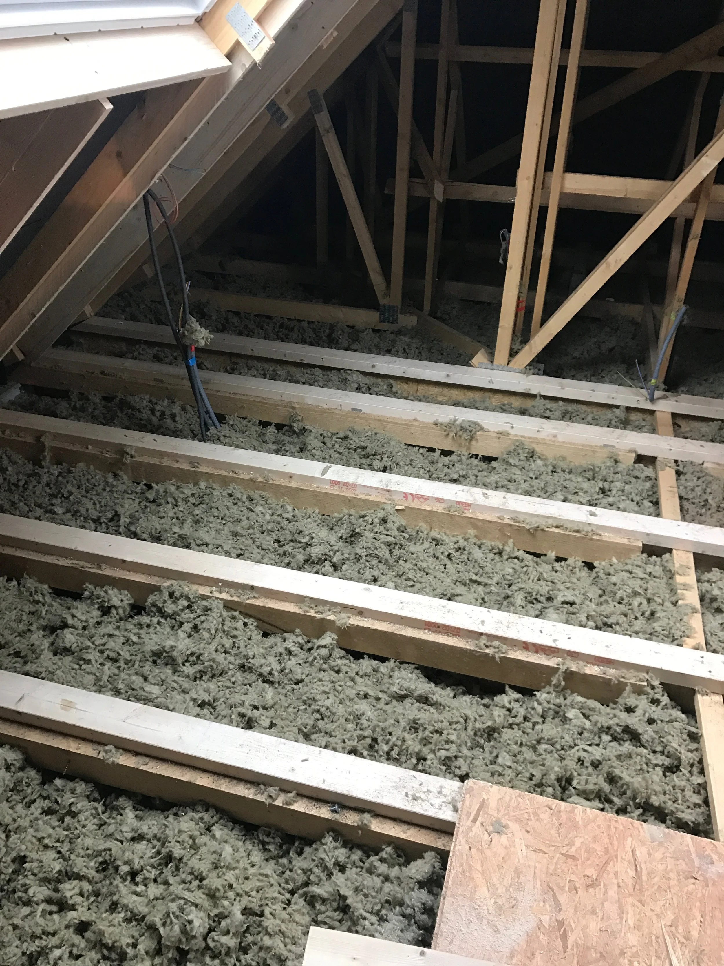 Une photo d'un toit en construction avec des poutres en bois et de la laine isolante éparpillée au sol.