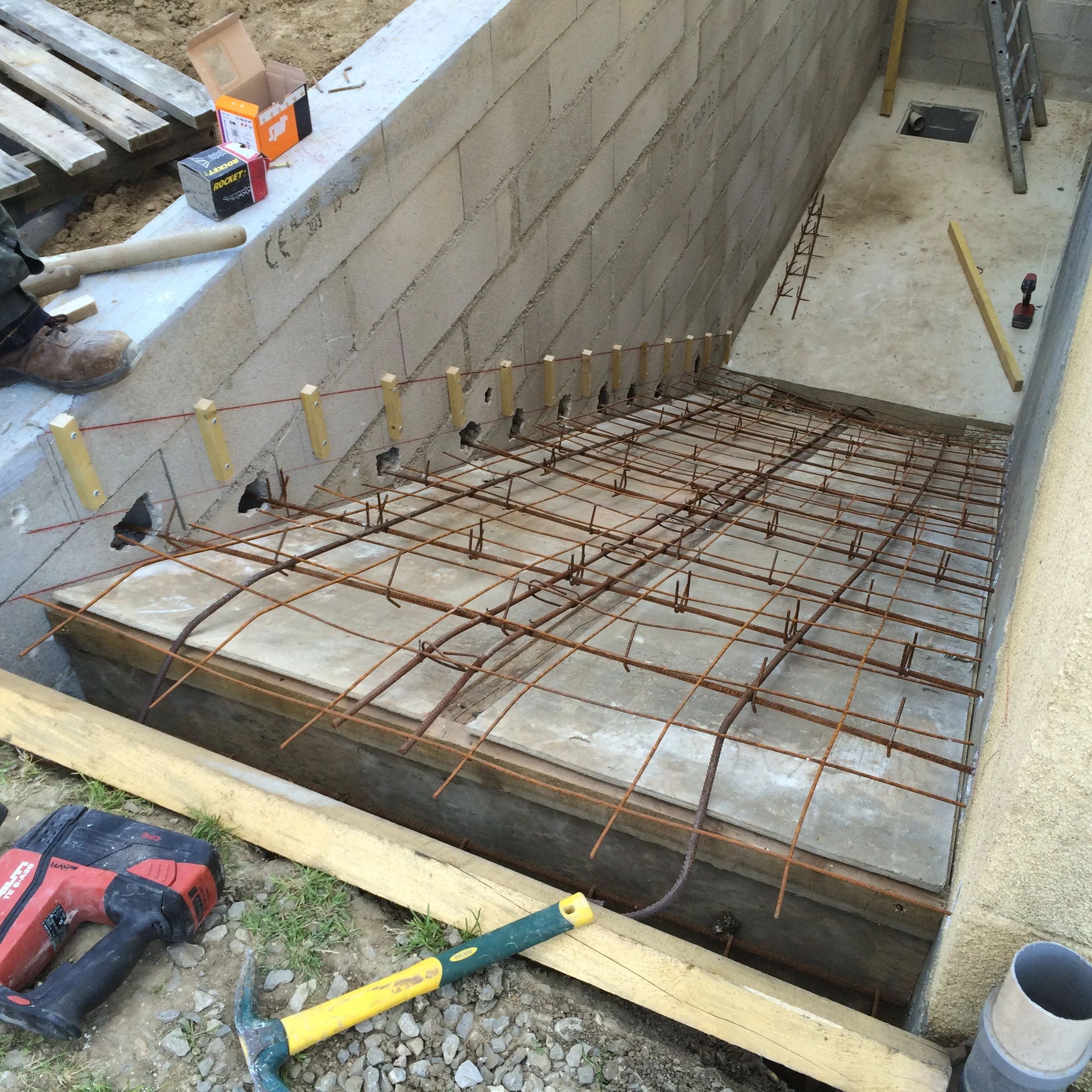 Construction d'un mur en parpaings avec armature en fer, outils de chantier et matériaux visibles.