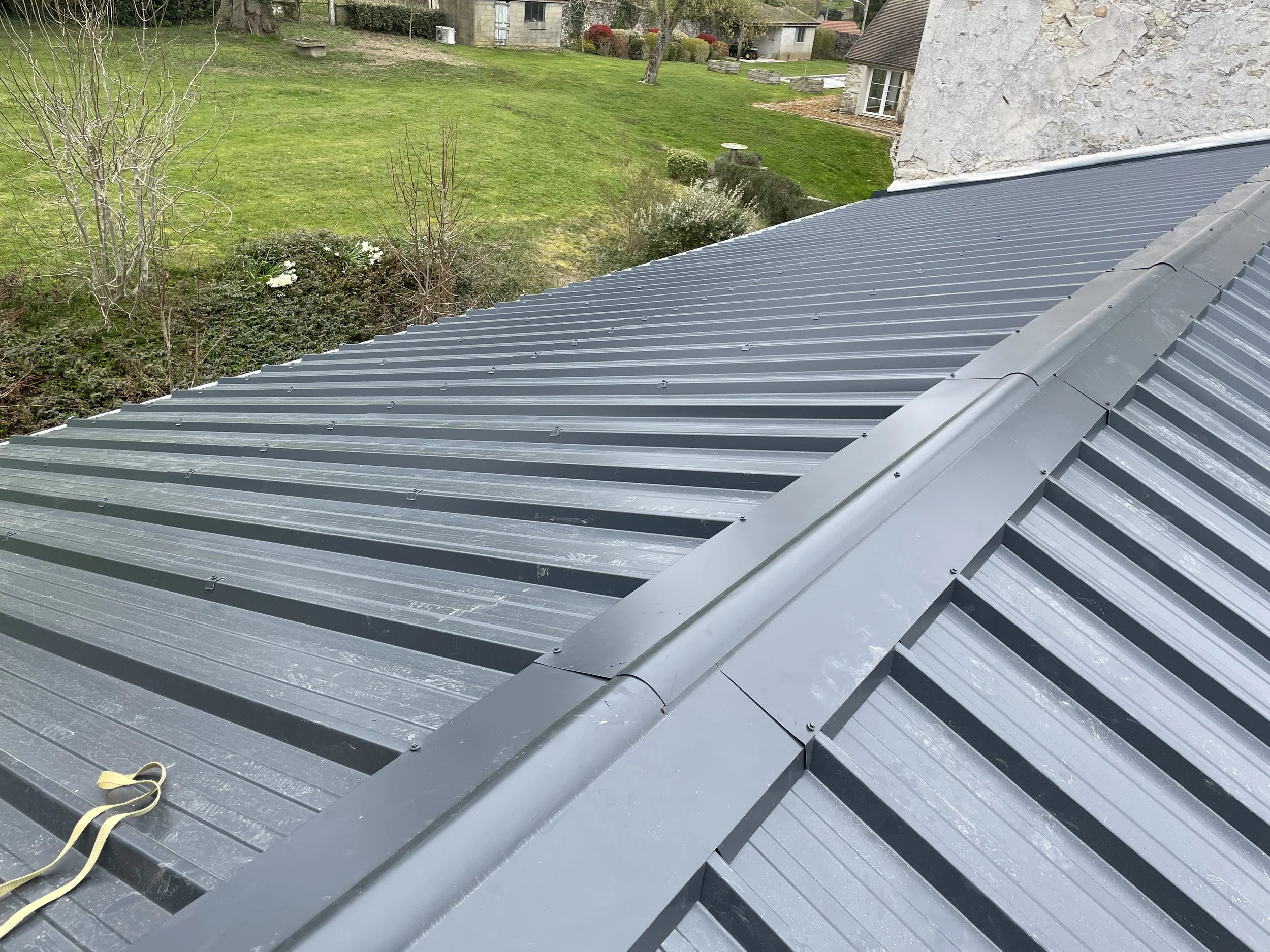 Toit en zinc installé (bac acier) sur une maison avec une pente, vue depuis le dessus, bordure du toit visible et jardin en arrière-plan.