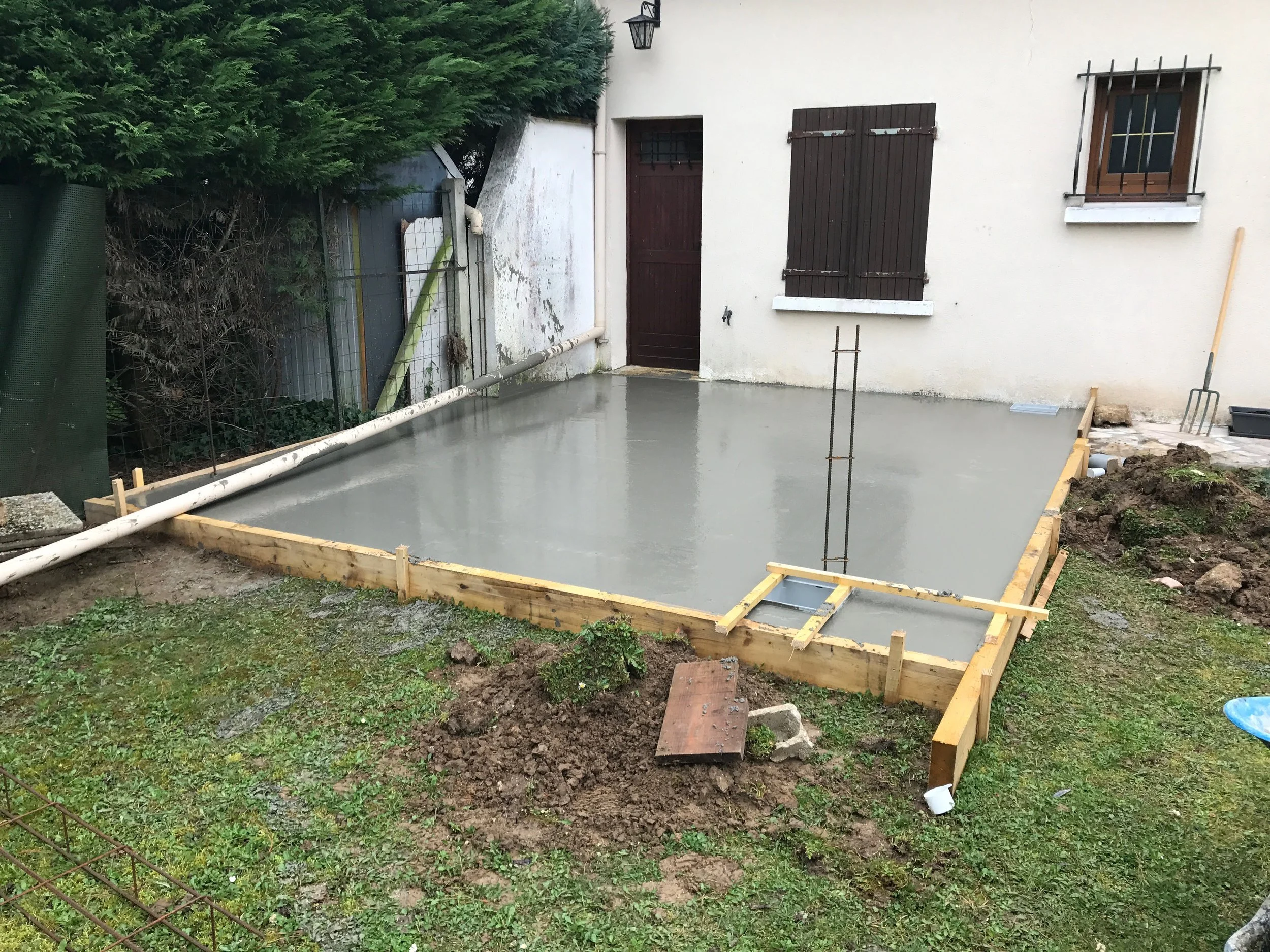 Travaux de construction avec une surface en béton fraîchement coulée, entourée d'une structure en bois.