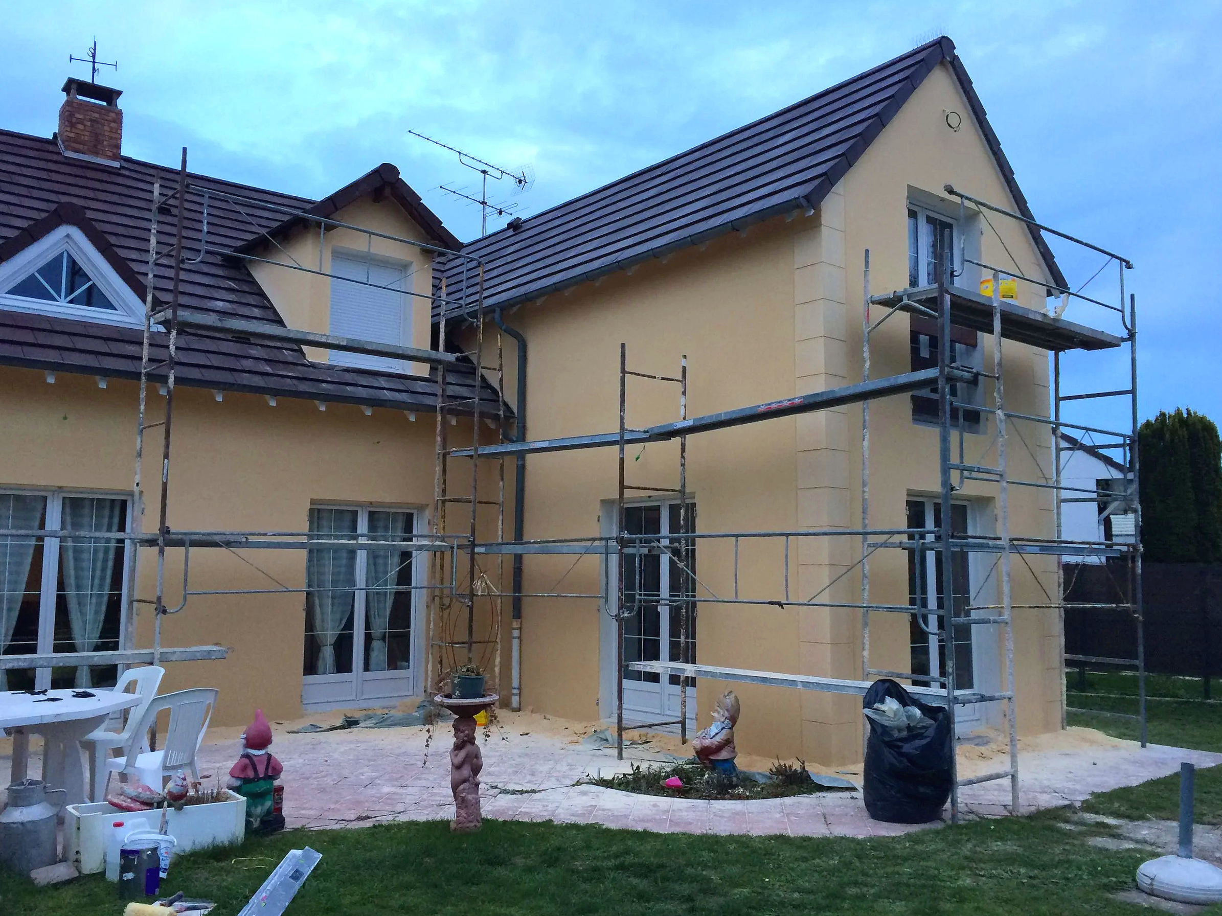 Une maison avec un toit en tuiles et des échafaudages installer sur la façade et le toit, indiquant des travaux de rénovation ou de construction.