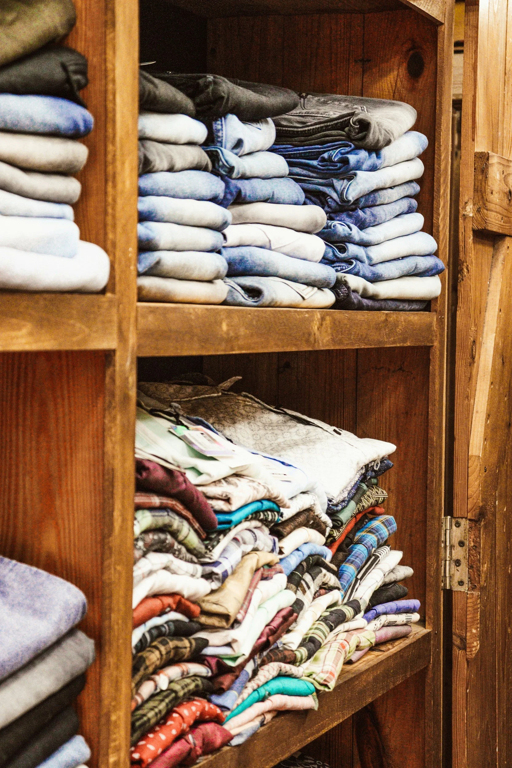 Wooden shelves filled with neatly folded jeans, shirts, and clothing items in various colors and patterns.