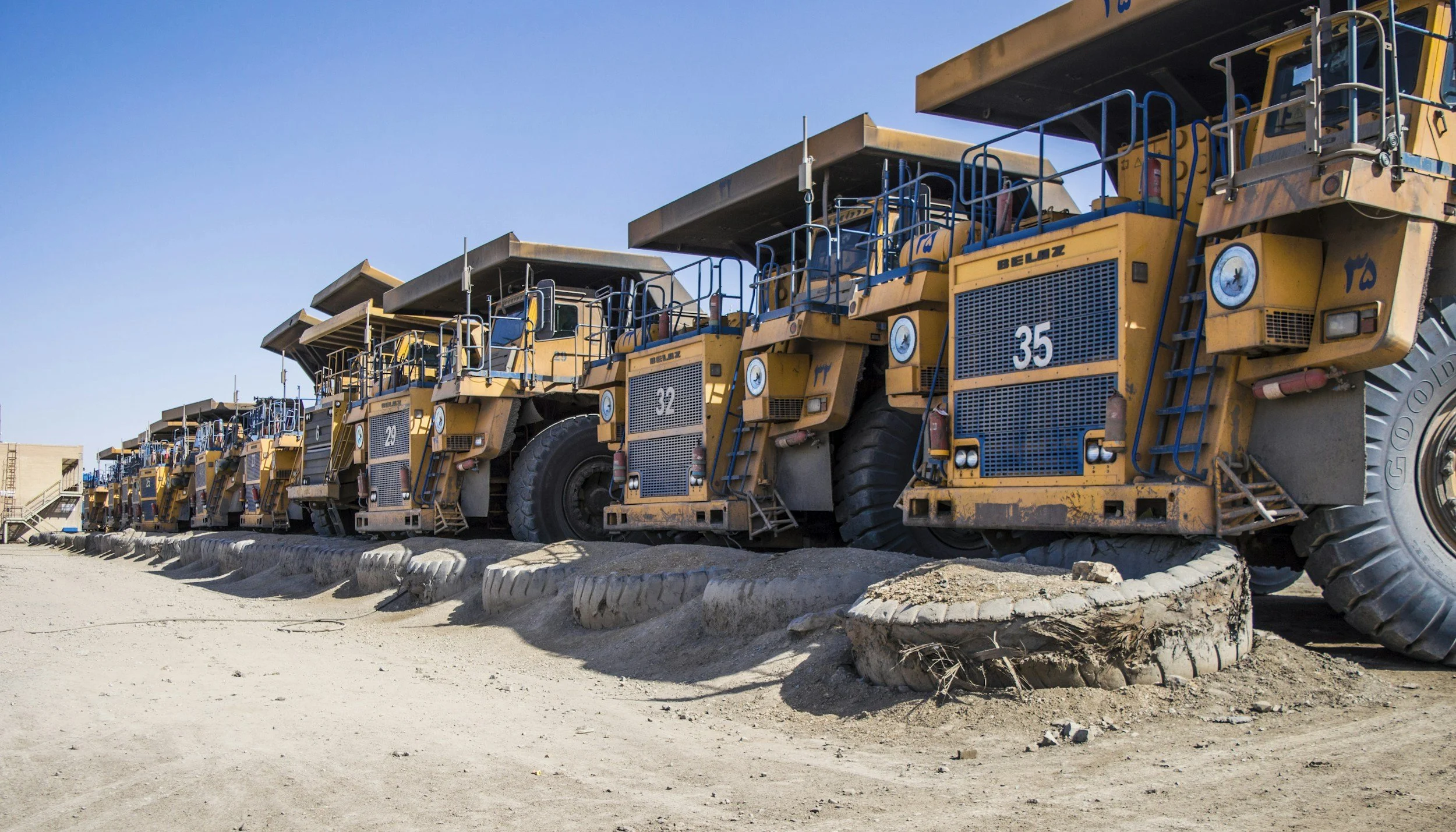 A row of yellow articulated dump trucks parked on a construction site under a clear blue sky.