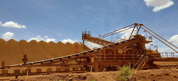Large industrial mining machine at a quarry with a conveyor belt, under a blue sky with clouds.