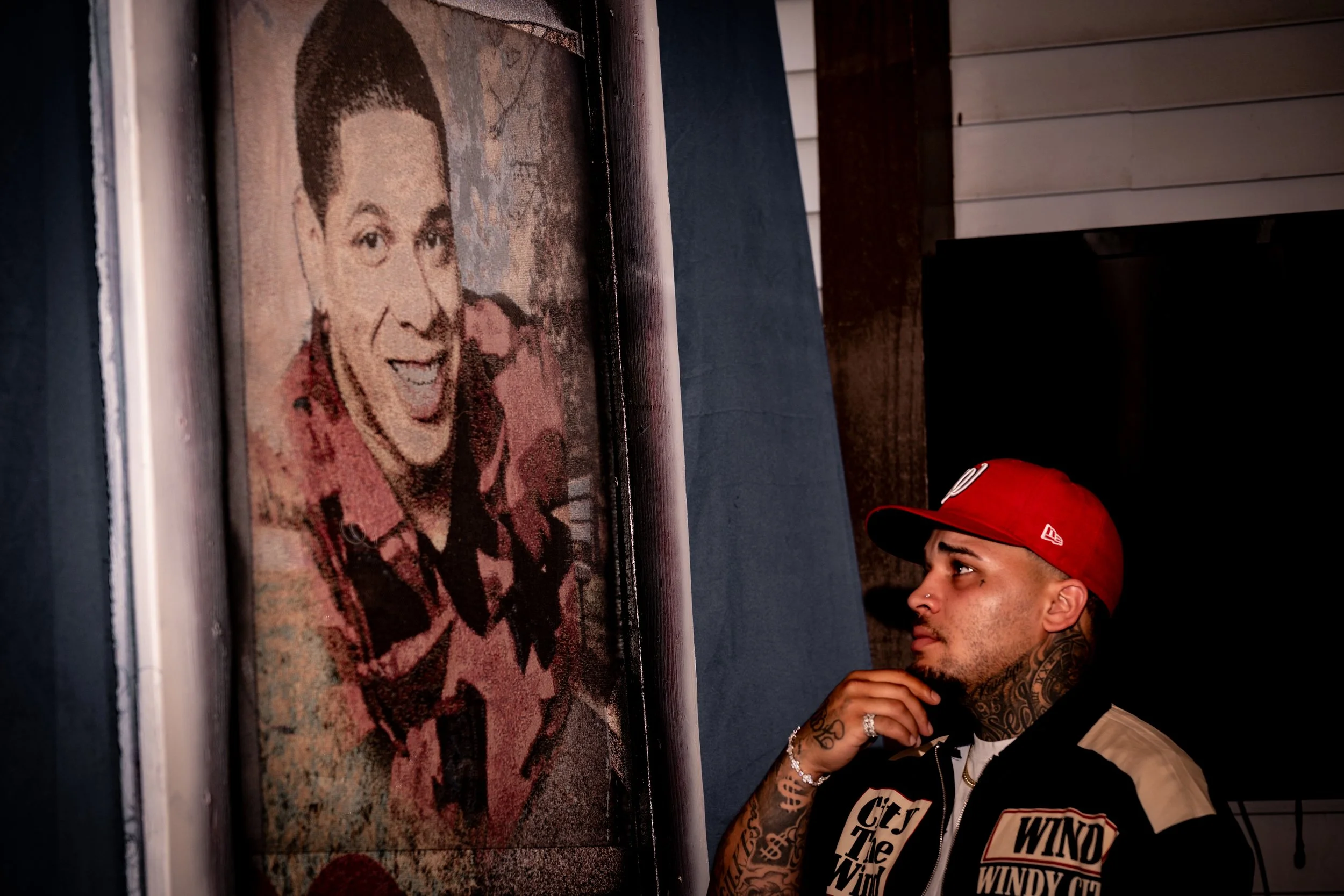 Young man with tattoos and a red cap looking at a large mosaic portrait of a smiling woman in an art gallery.