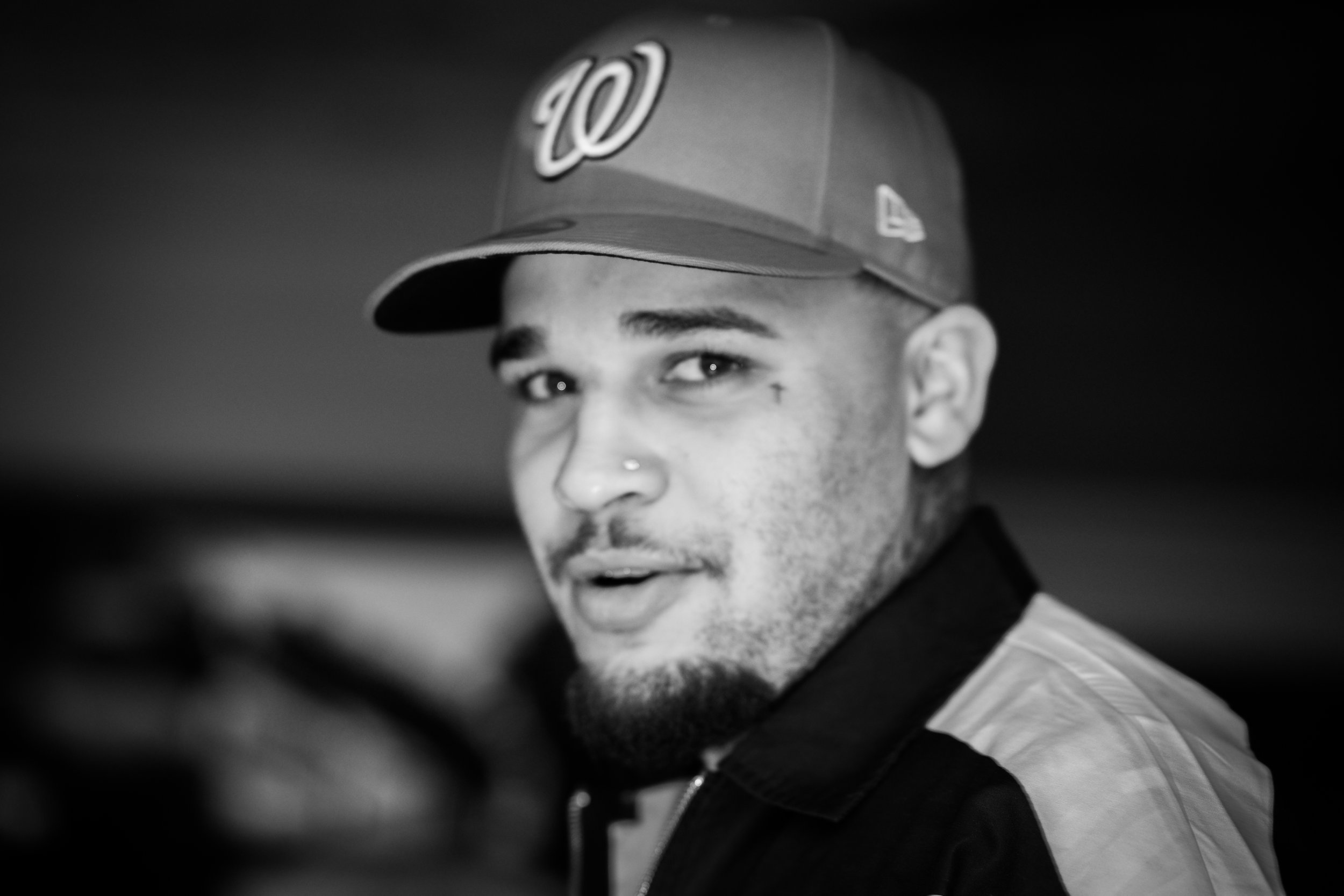 Black and white photo of a young man wearing a baseball cap with a 'W' logo, looking into the camera with one eye visible and a surprised or excited expression.