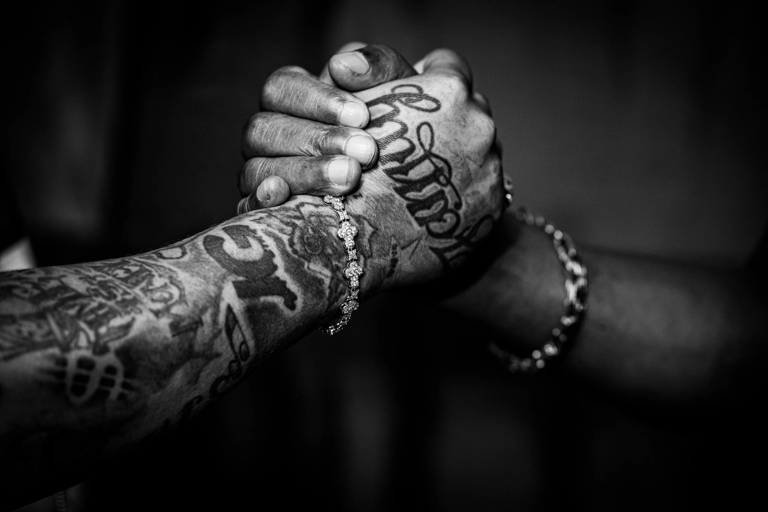 Close-up of two tattoos on a person's arms, with the hands clasped together; one hand is wearing a sparkling bracelet, in black and white.