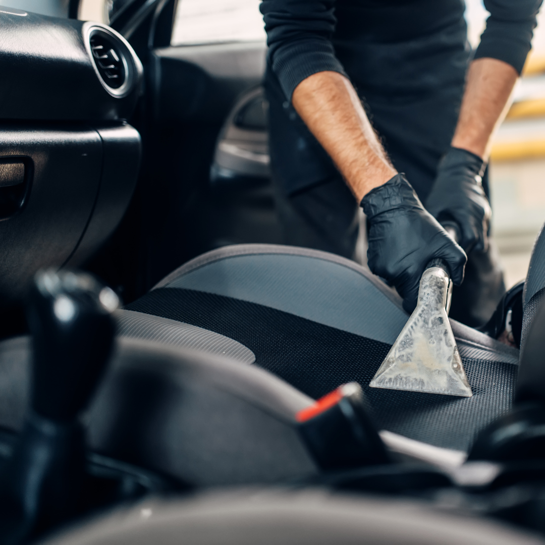 Person wearing black gloves cleaning car seat with a cloth inside vehicle