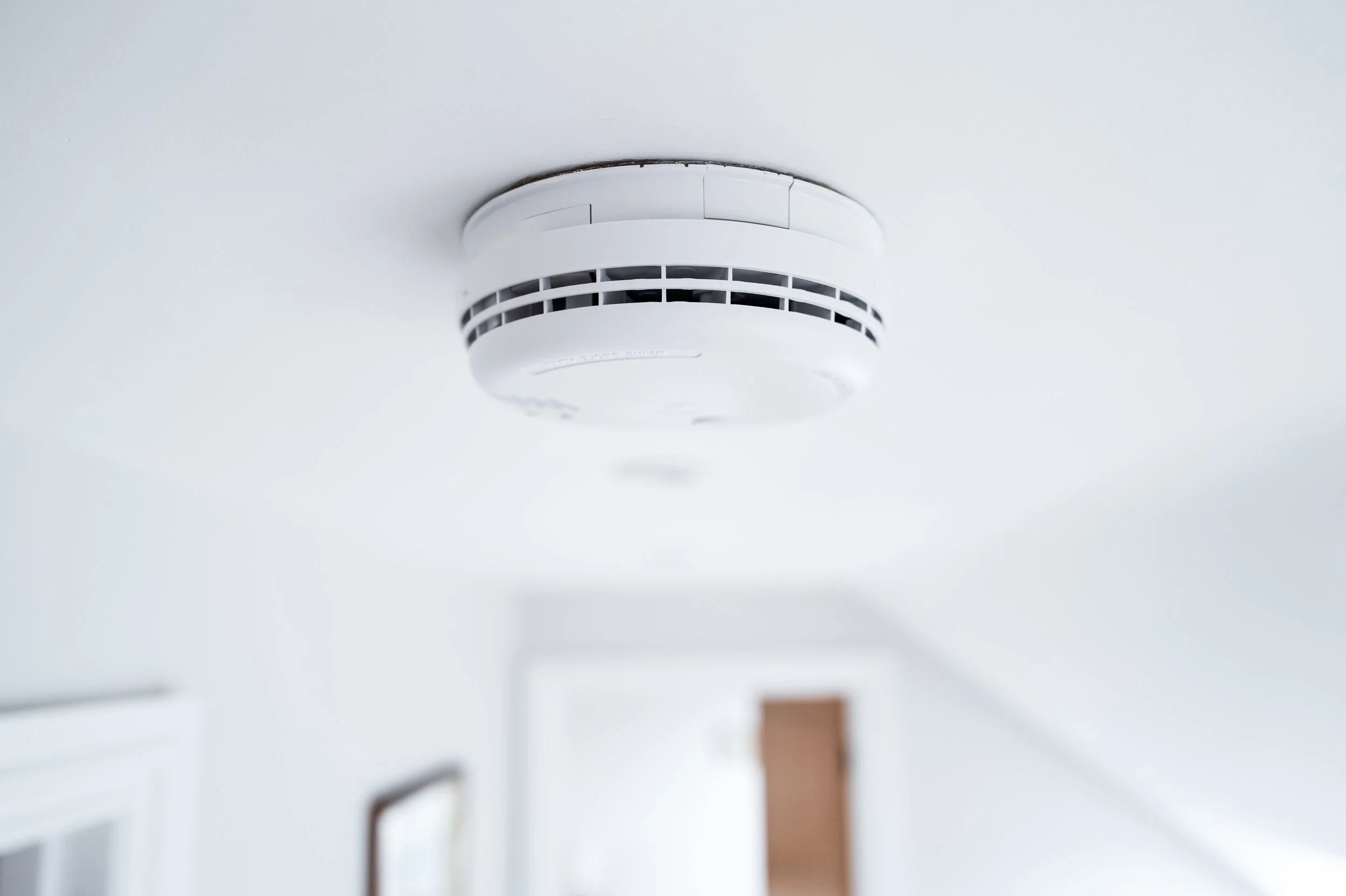 Close-up of a white smoke alarm mounted on a white ceiling in a room with minimal decor.