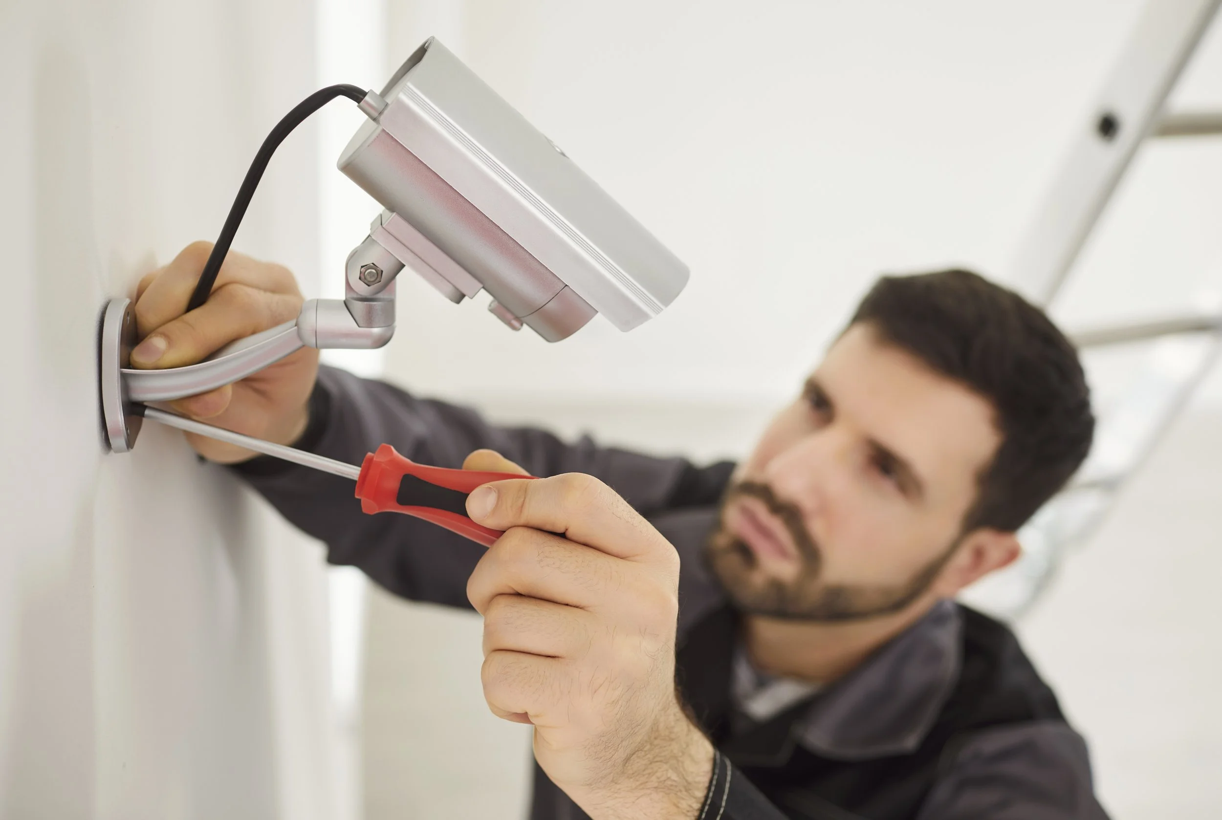 A man using a screwdriver to install or repair a device on a wall, with a focus on the screwdriver and device.