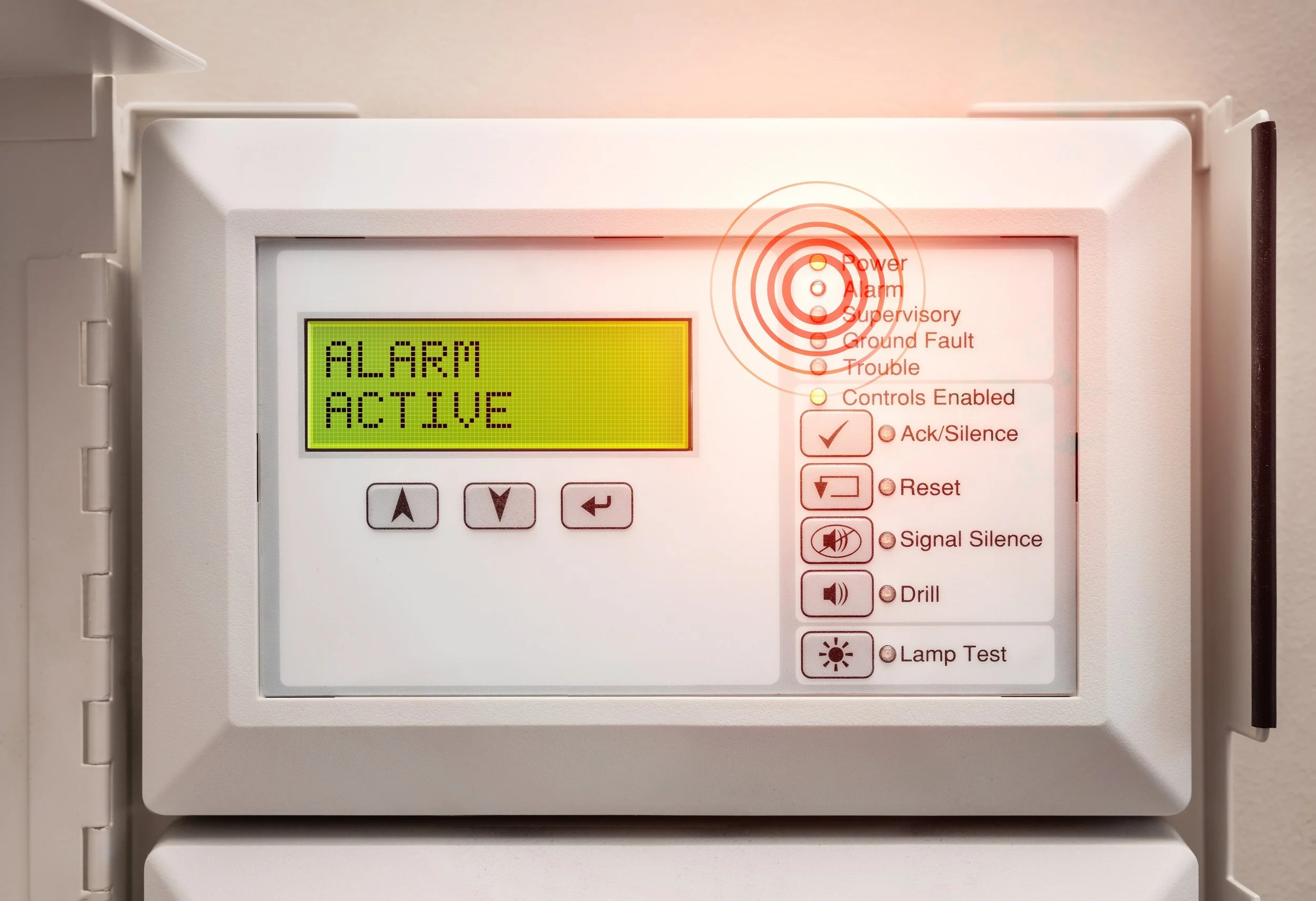 A white electrical panel with a small digital display reading 'ALARM ACTIVE.' To the right, there are indicator lights with labels, including 'Power,' 'Alarm,' 'Supervisory,' 'Ground Fault,' and 'Trouble.' The panel has control buttons and labels for functions like 'Acknowledgment/Silence' and 'Reset.'