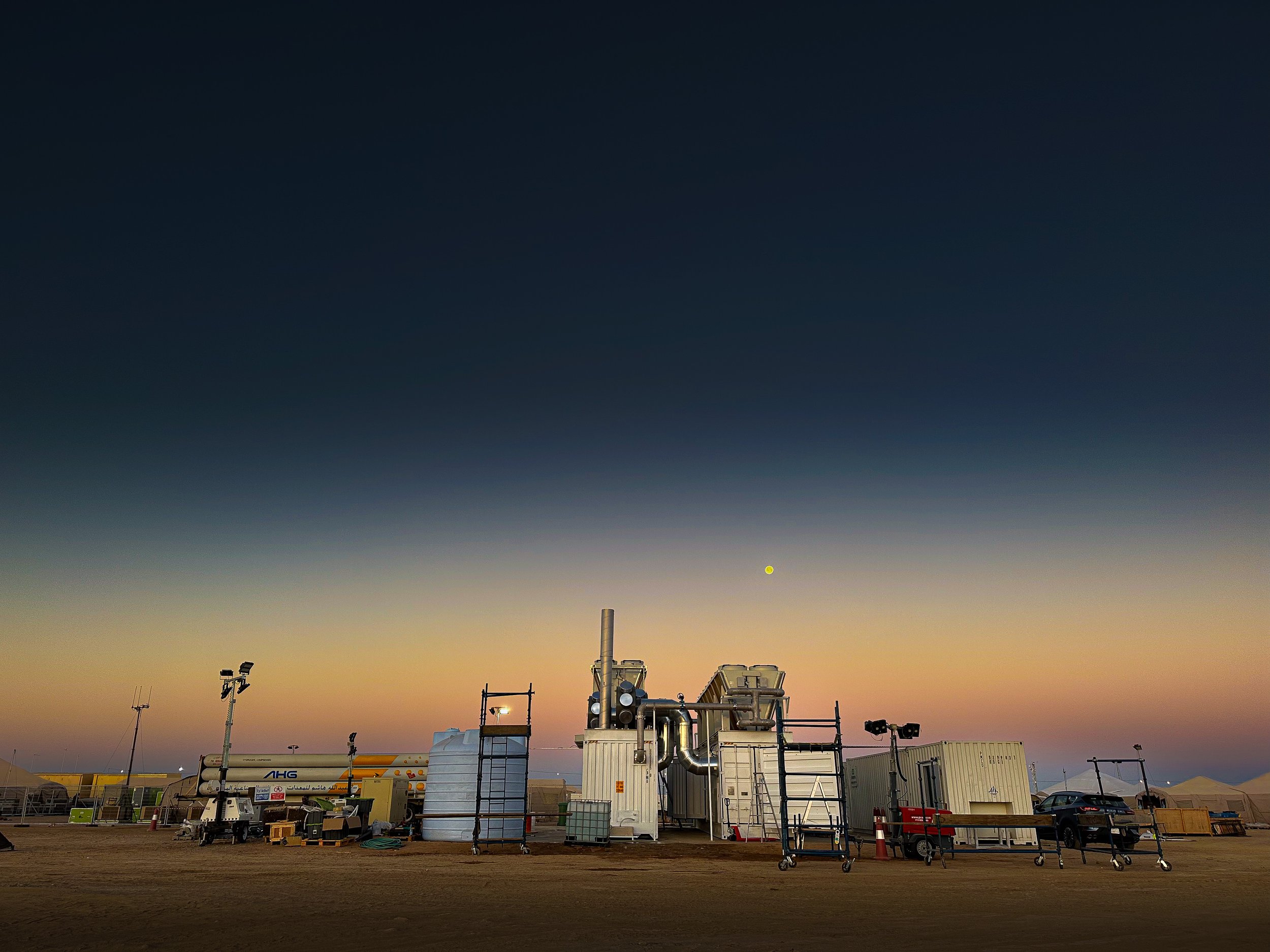 View of industrial equipment and containers at an outdoor site during sunset, with a clear sky and distant mountains. This is the NEOM site in Saudi Arabia where Energys delivered a 1MW scale containerised power system.