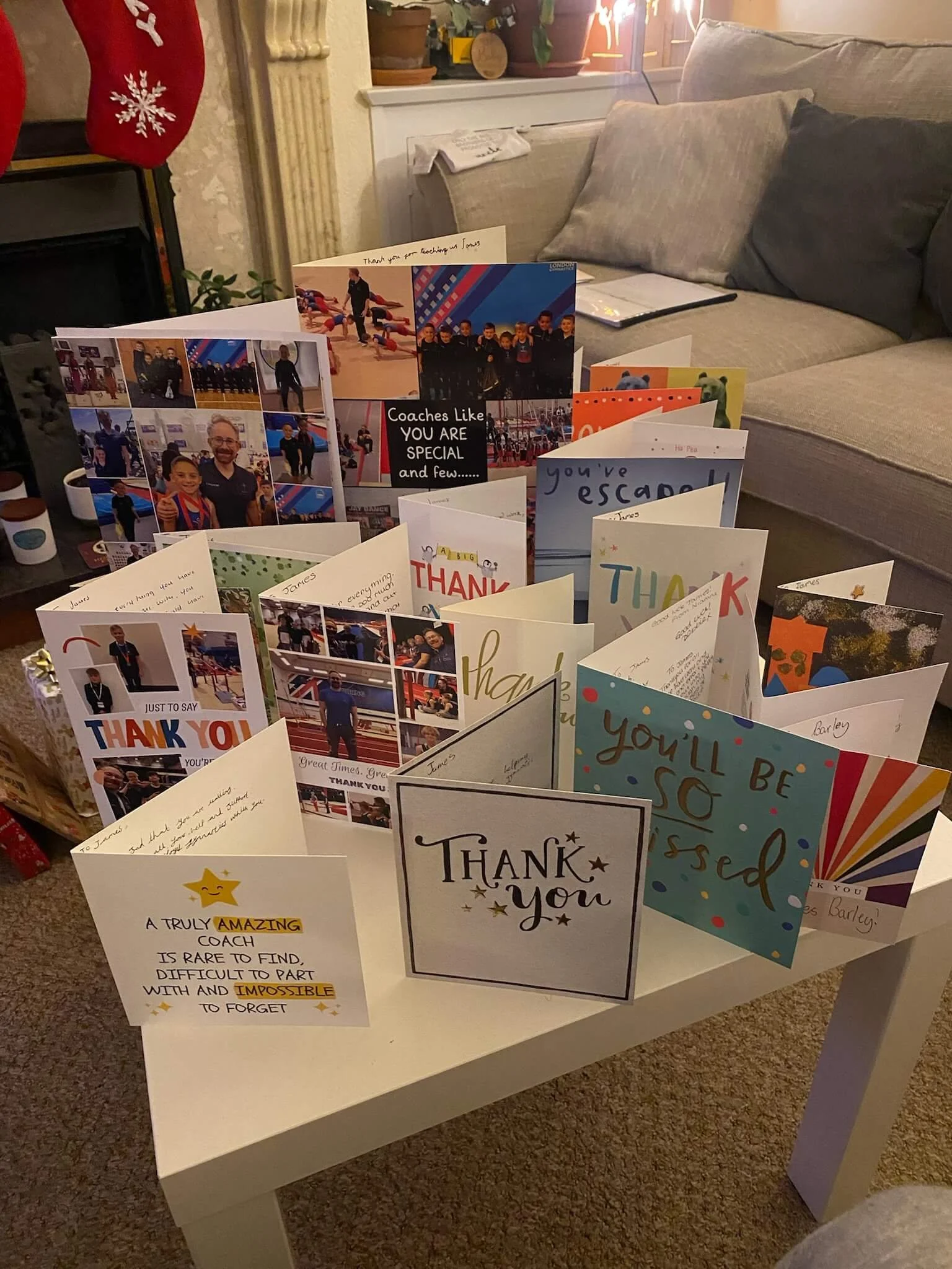 A collection of thank you cards arranged on a table in a cozy living room. The cards feature various designs, photos, and handwritten messages.