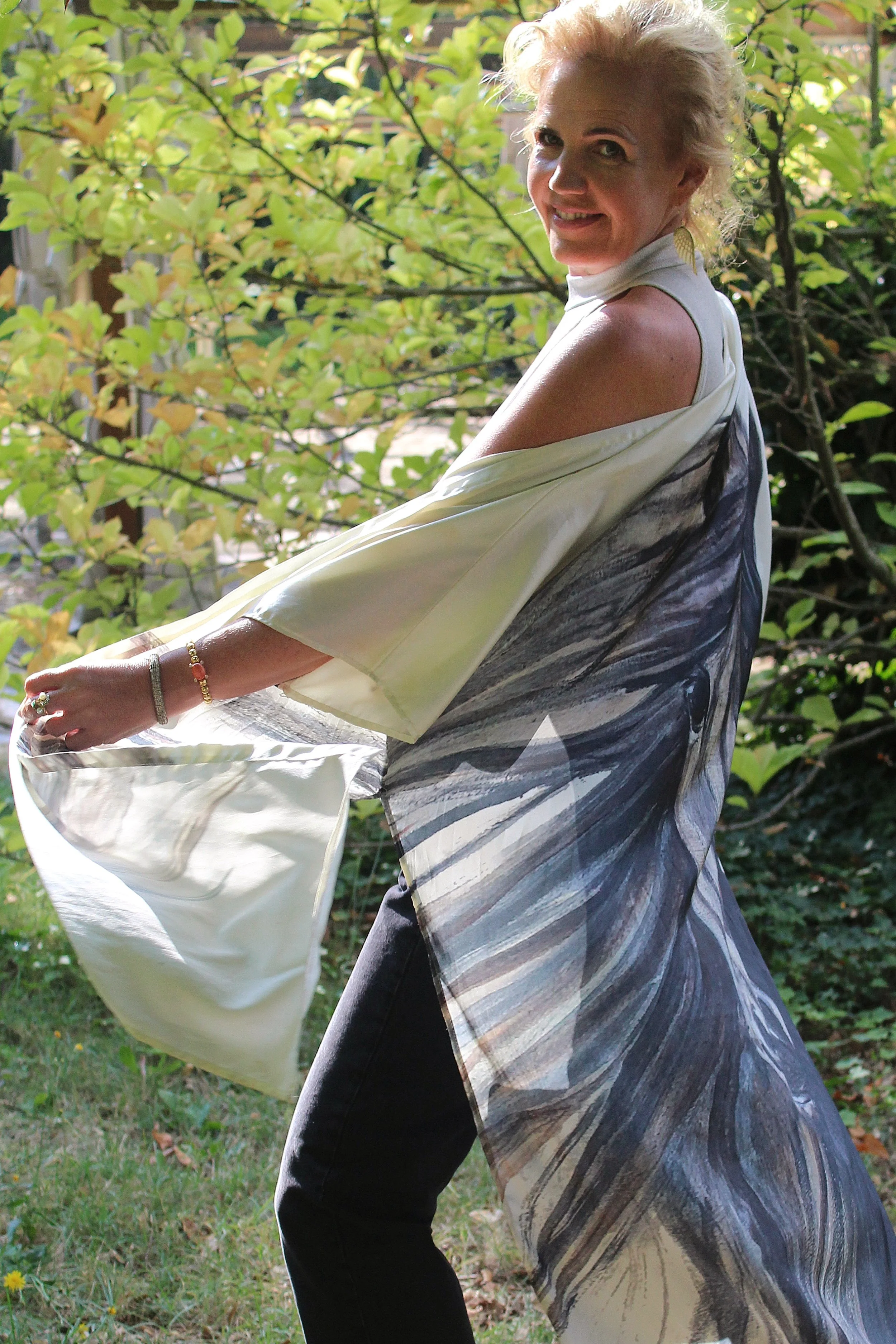 A smiling woman with blonde hair in an outdoor setting with greenery, feeling happy.