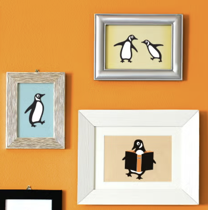 Decorative framed artwork featuring penguin illustrations on an orange wall.