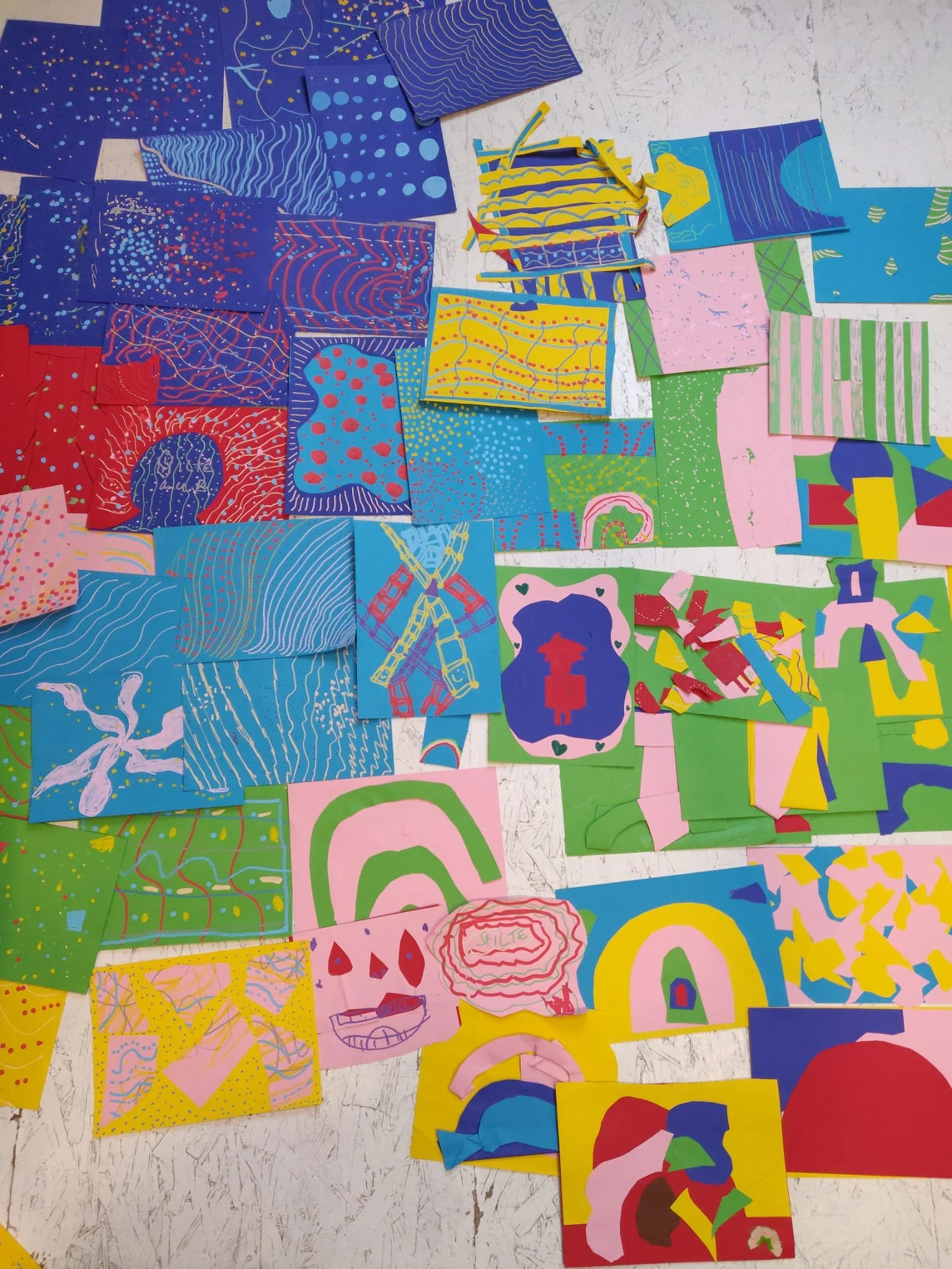 Colorful abstract drawings and cut-out shapes on paper spread across a white textured surface.