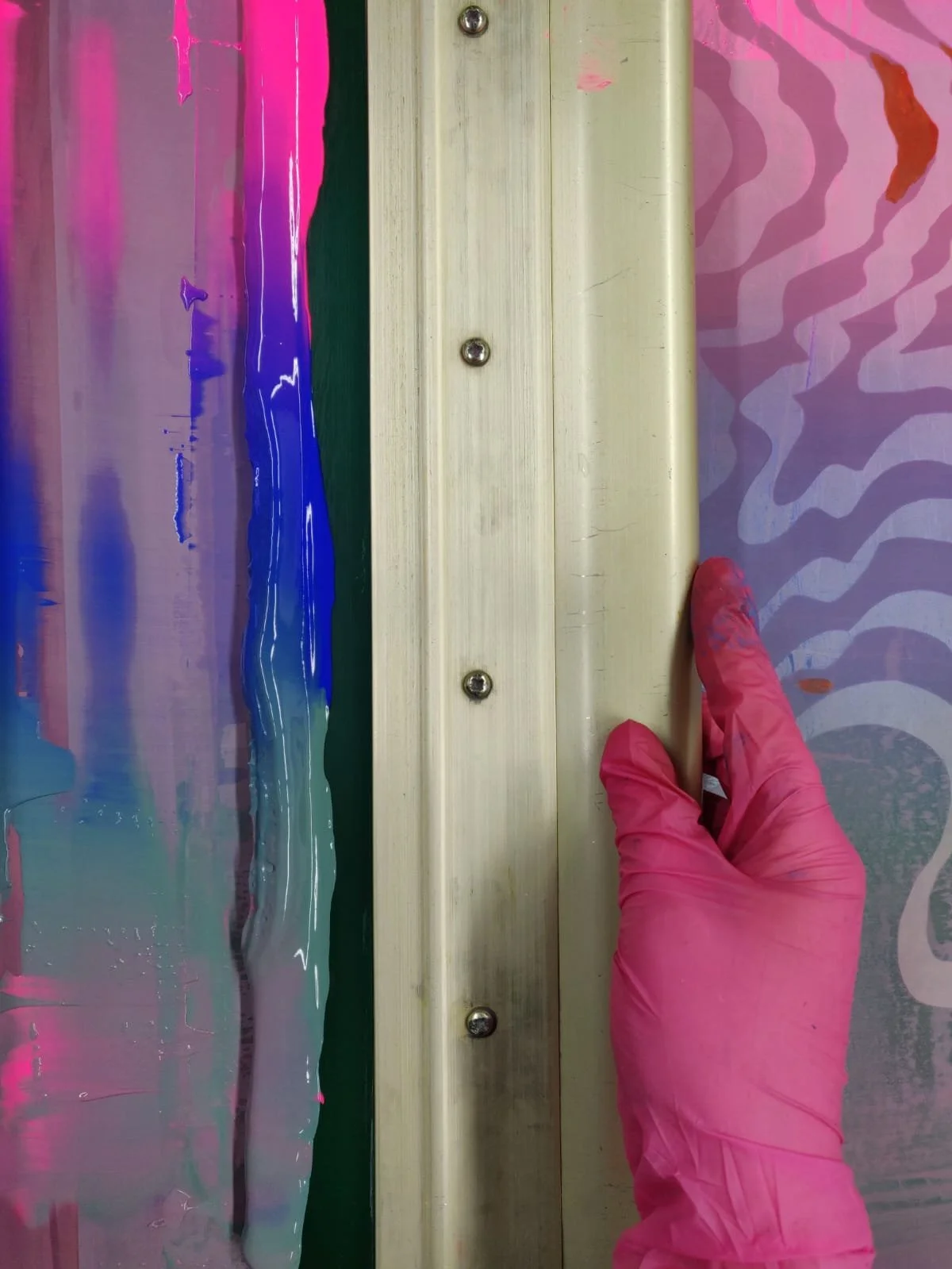 A hand wearing a pink glove holding a strip of reflective material with a wood piece and screws attached, with colorful abstract background.