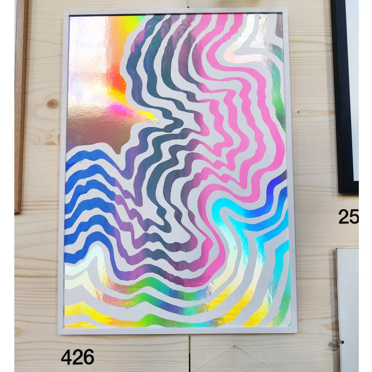 Holographic artwork with multicolored wavy lines on a white background, mounted on a wooden surface.