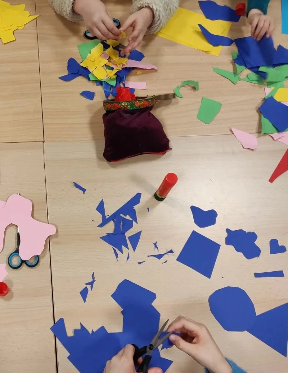 Children cutting and gluing colorful paper shapes during an arts and crafts activity at a table.
