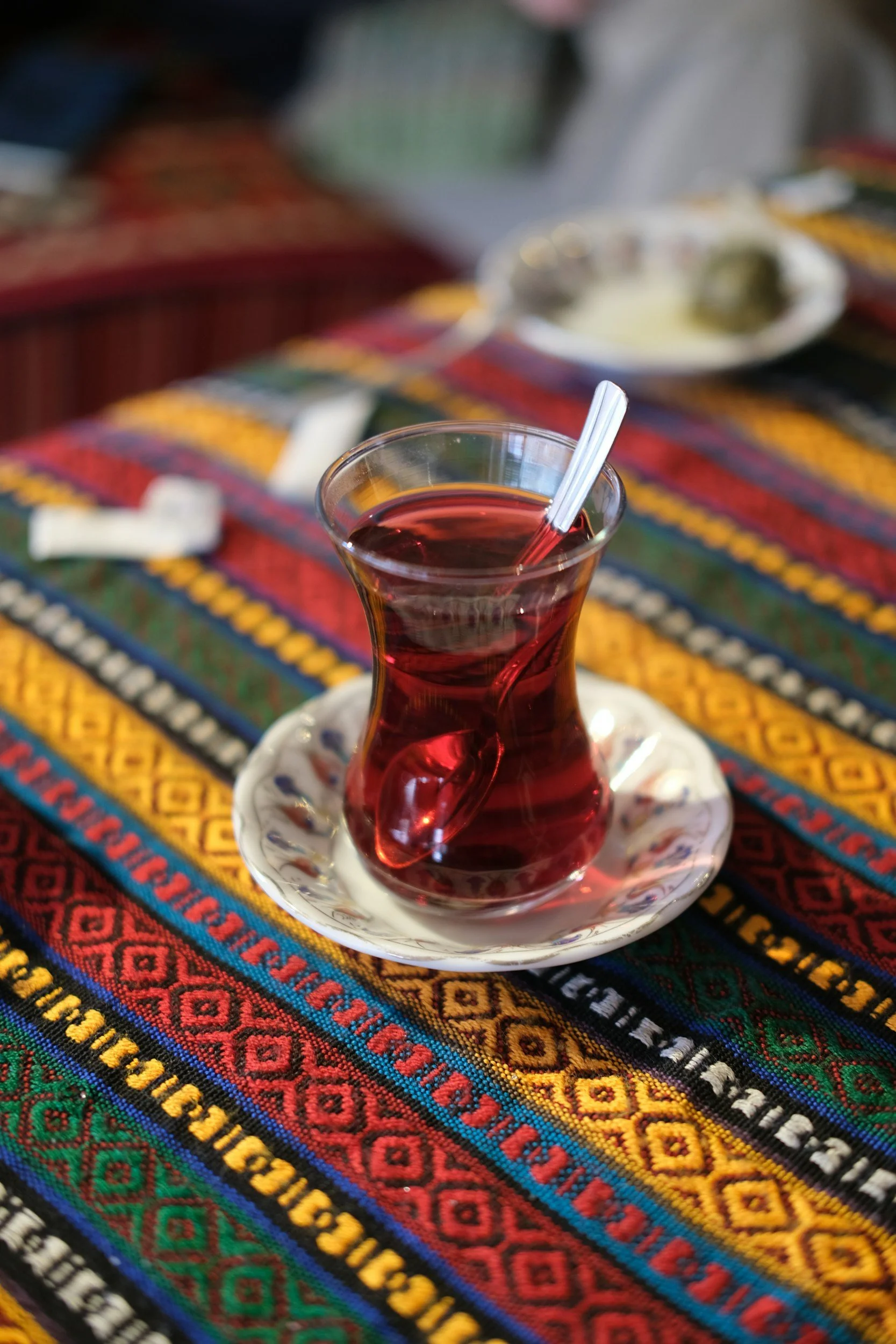 Renkli geleneksel el dokuması masa örtüsü üzerinde bir çay bardağı ve buna takılı ince bir pipet yer alıyor.