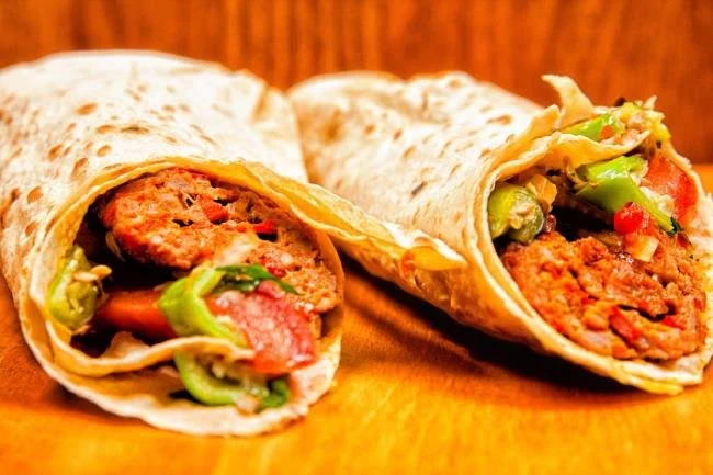 İki dürüm taco, içi kıyma, domates, yeşil biber ve salata ile doldurulmuş, yan yana duruyor.