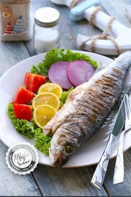 Porsiyonluk balık ve garnitür içeren tabak, yanında salata ve limon dilimleri, arka planda tuz ve baharat kapsülleri ve baharat kutusu.