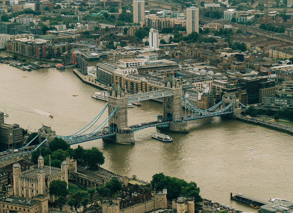Aerial view of Tower Bridge over the River Thames in London, with surrounding city buildings and boats on the water.