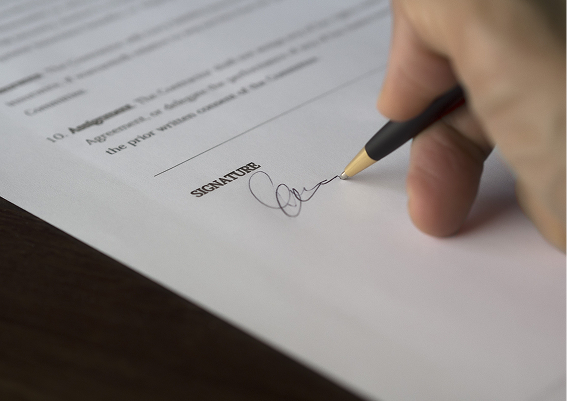 Close-up of a hand signing a document with a black pen.