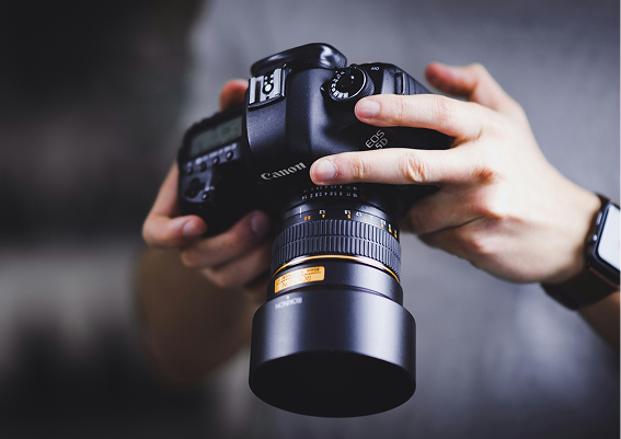 Person holding a Canon DSLR camera with a telephoto lens.