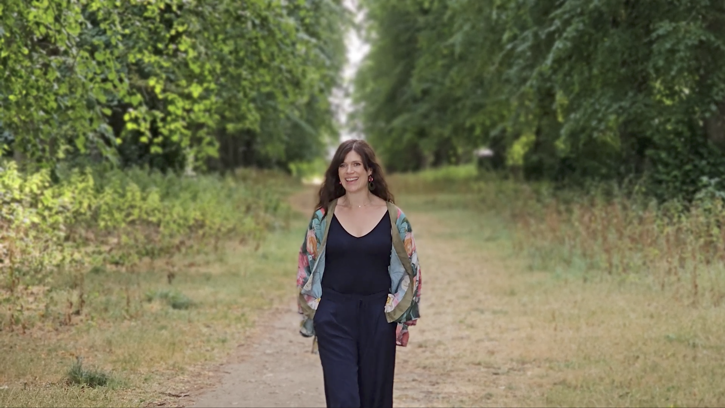 Katie, founder of Optimise, walking along a tree-lined path.