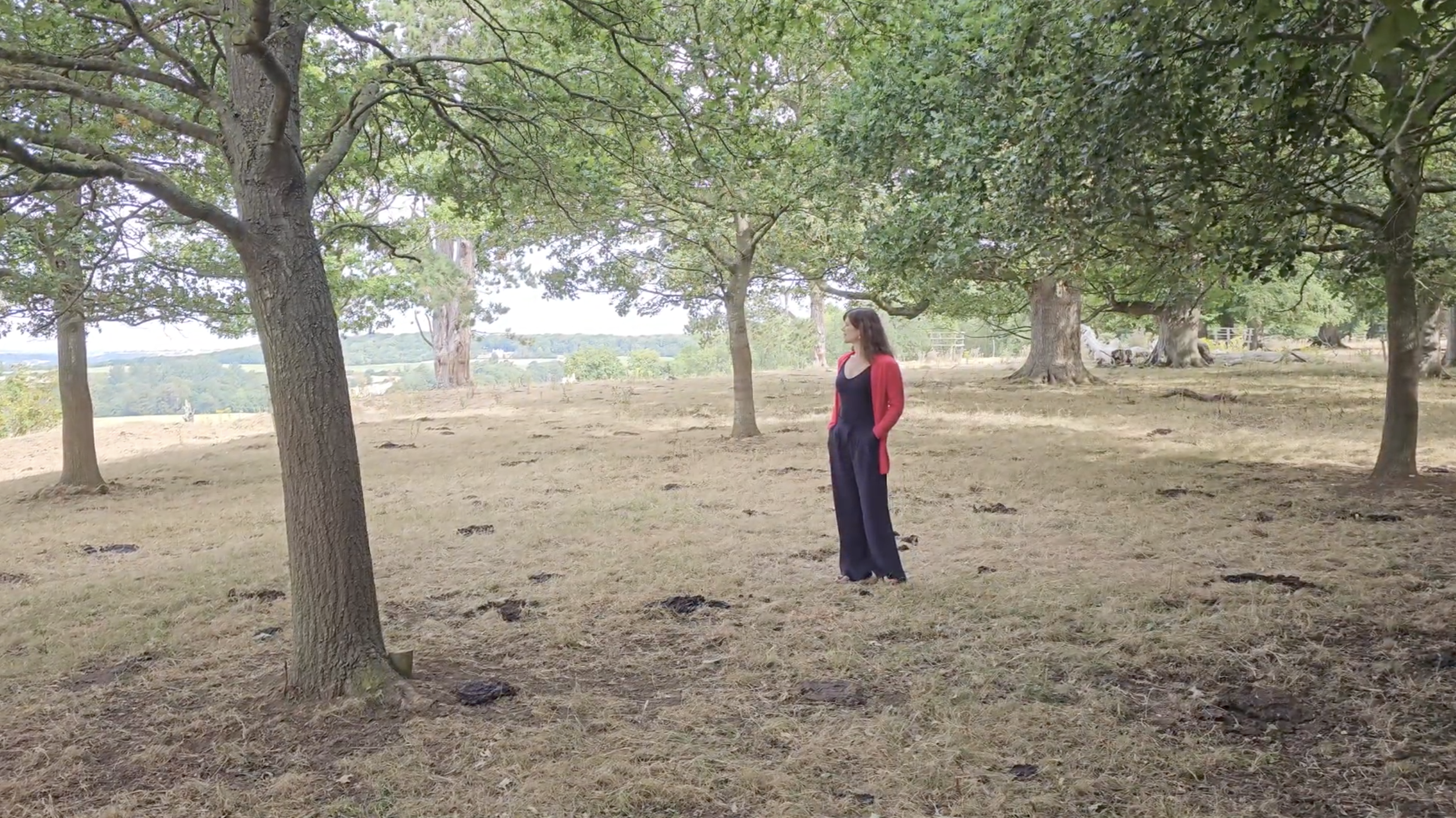 Katie standing among mature trees in an open natural landscape.