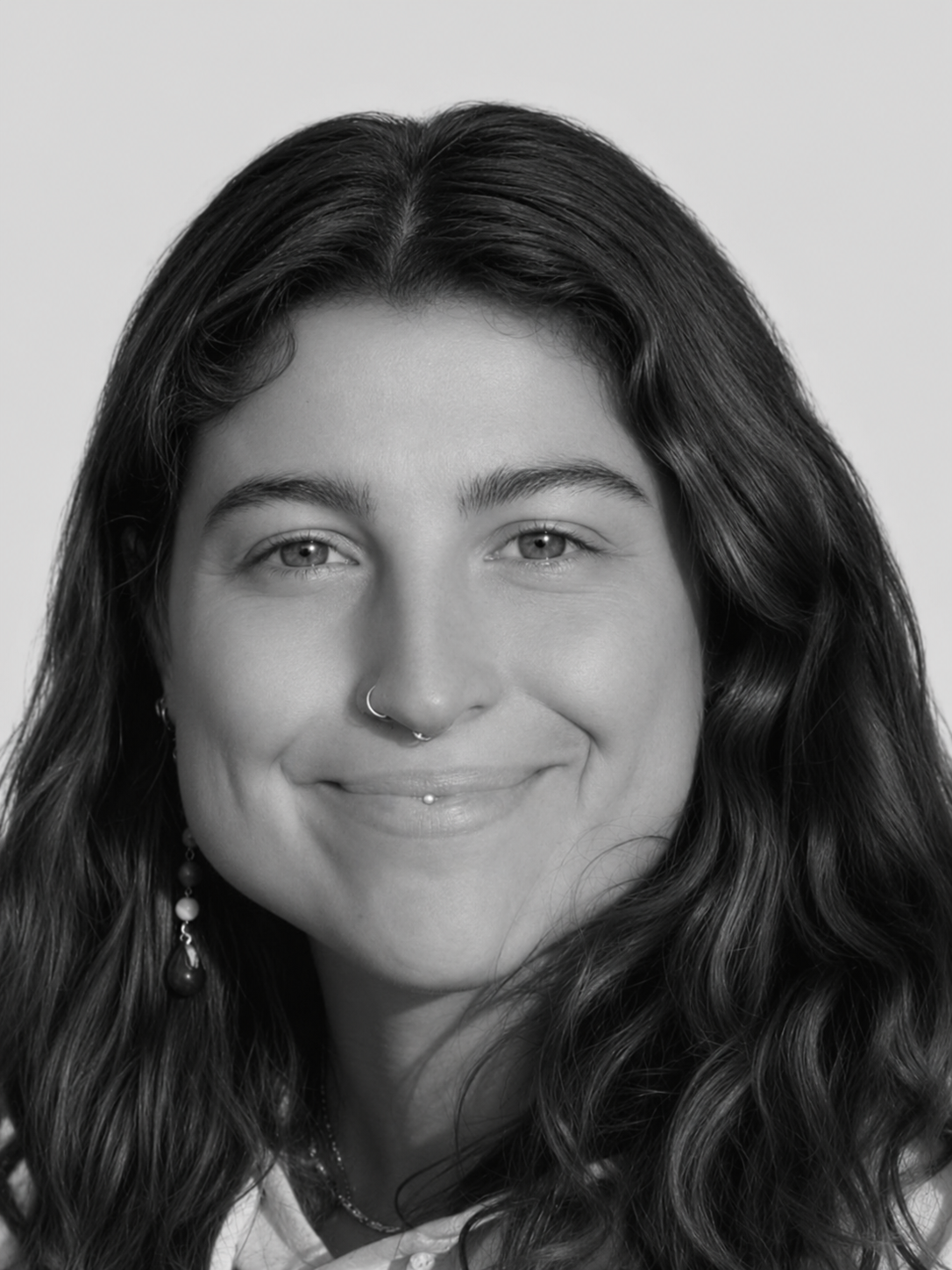 Close-up black and white portrait of a young woman with long, wavy hair smiling at the camera.