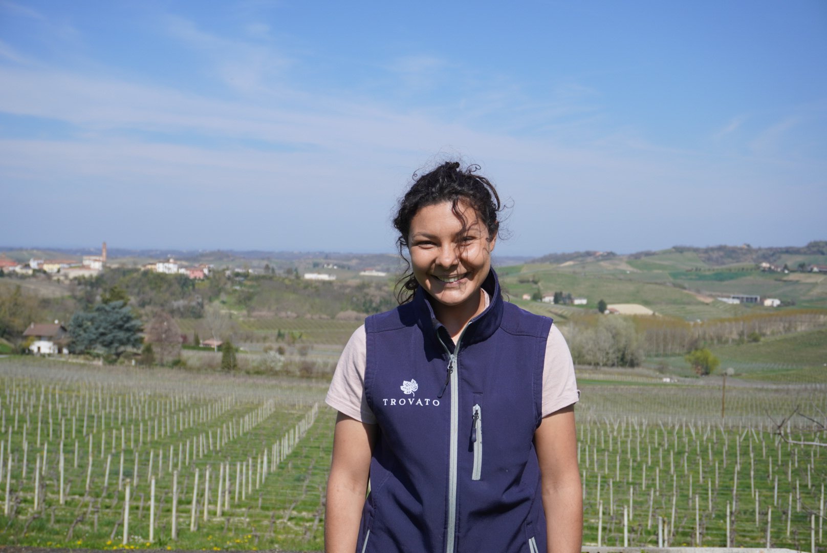 Donna sorridente in un vigneto con paesaggio collinare e costruzioni in lontananza
