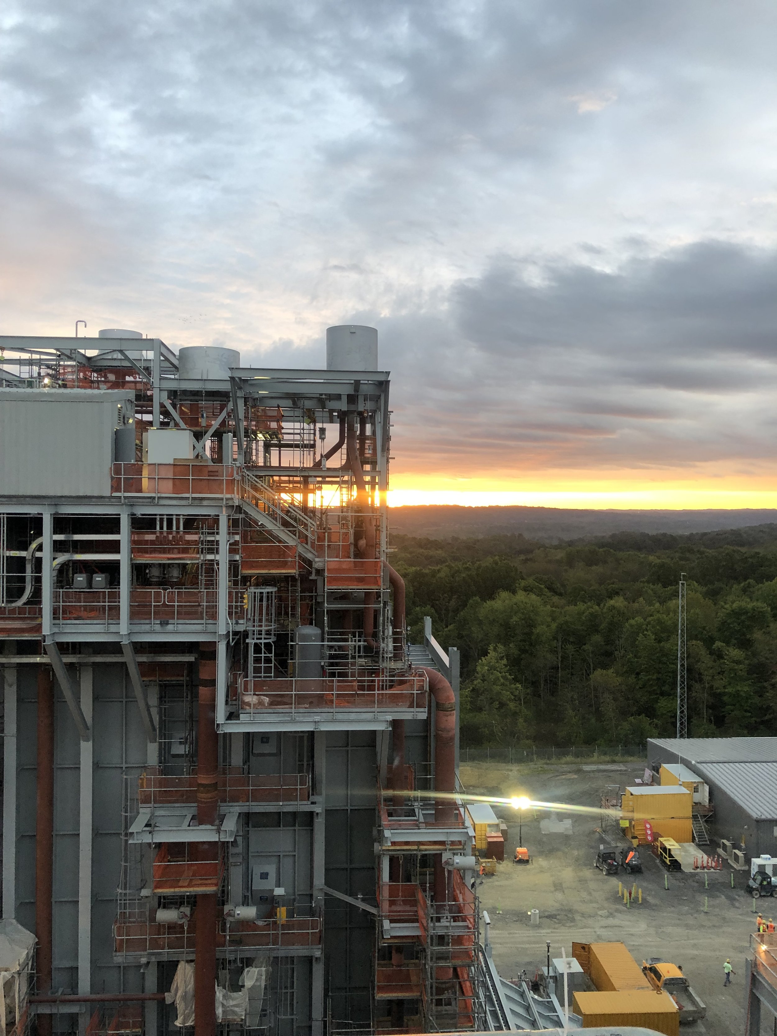 Construction site with industrial equipment and a sunset sky with clouds in the background.