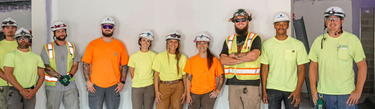 A group of construction workers and engineers standing together inside a building site, wearing safety helmets and high-visibility shirts.