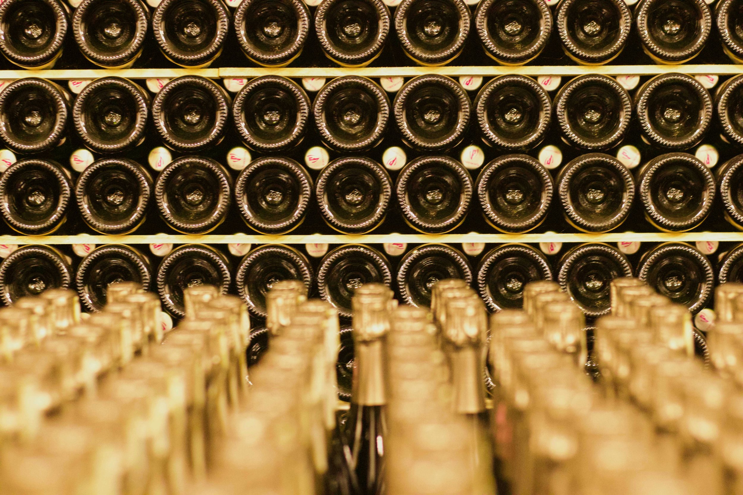 A display of multiple bottles from a wine or champagne collection, arranged on shelves in a store or winery.