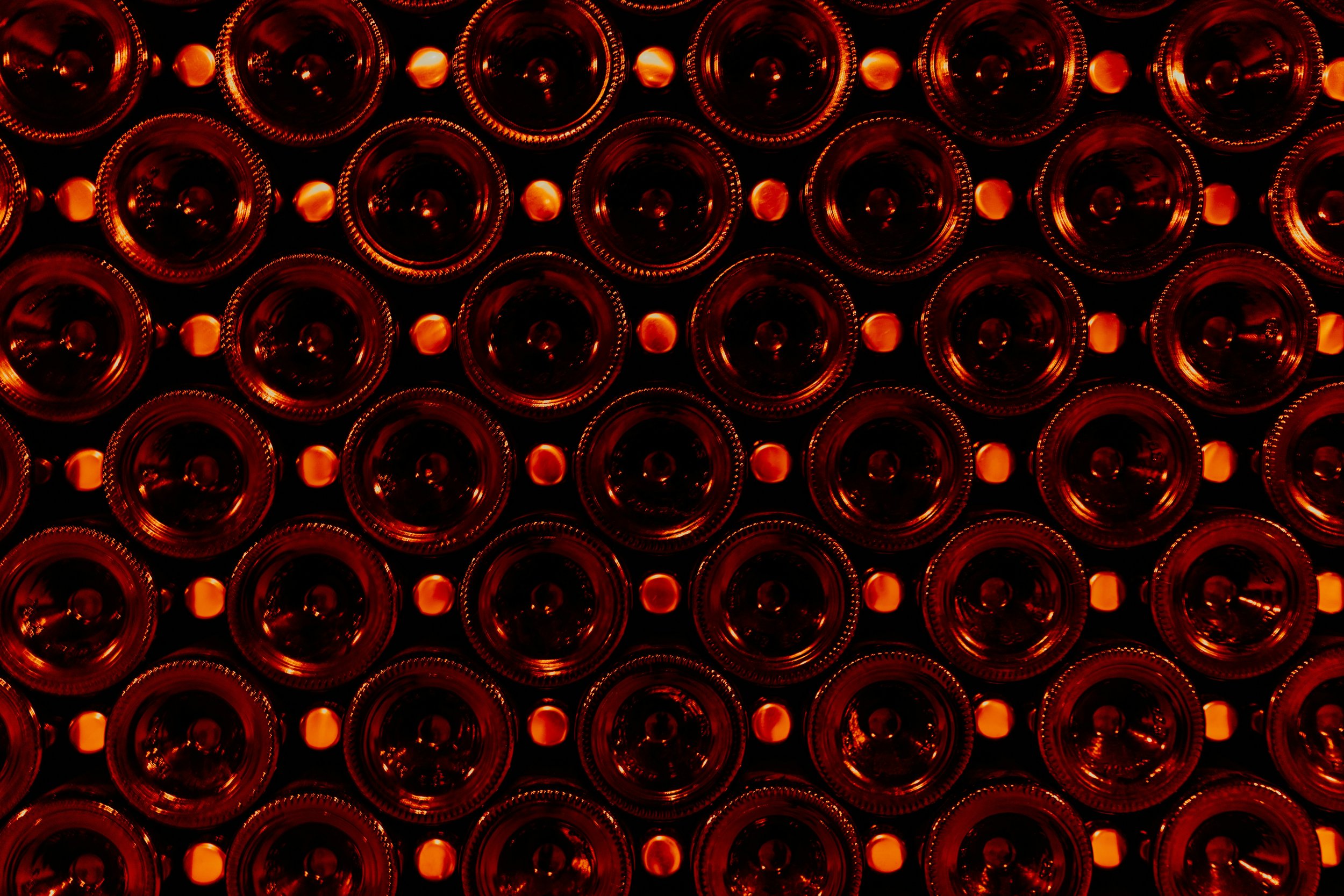 A pattern of numerous red glass bottles viewed from the bottom, laying horizontally, illuminated with red lighting.