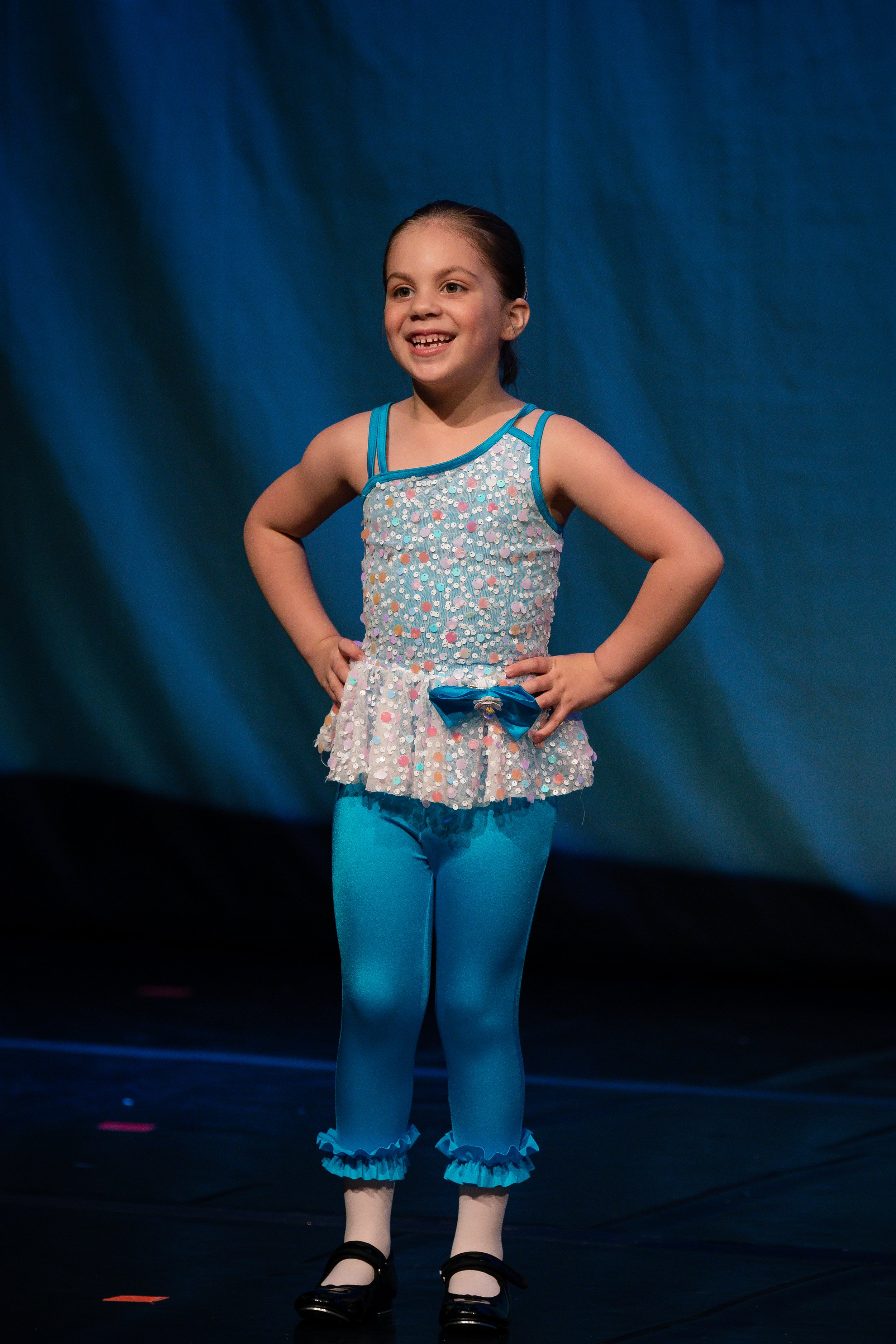 Young girl in a colorful dance costume standing with hands on hips on stage.